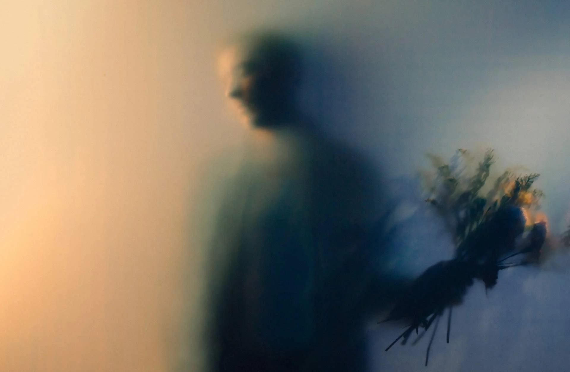 A blurred silhouette of a person holding a bouquet of flowers against a gradient background.
