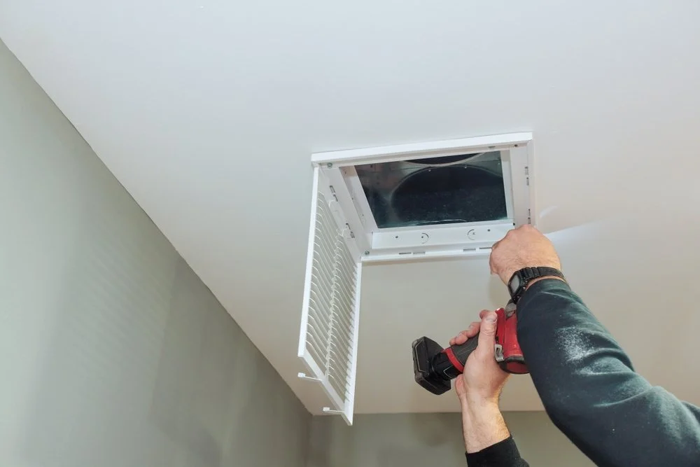 Person installing or repairing attic vent with a cordless drill on a ceiling.
