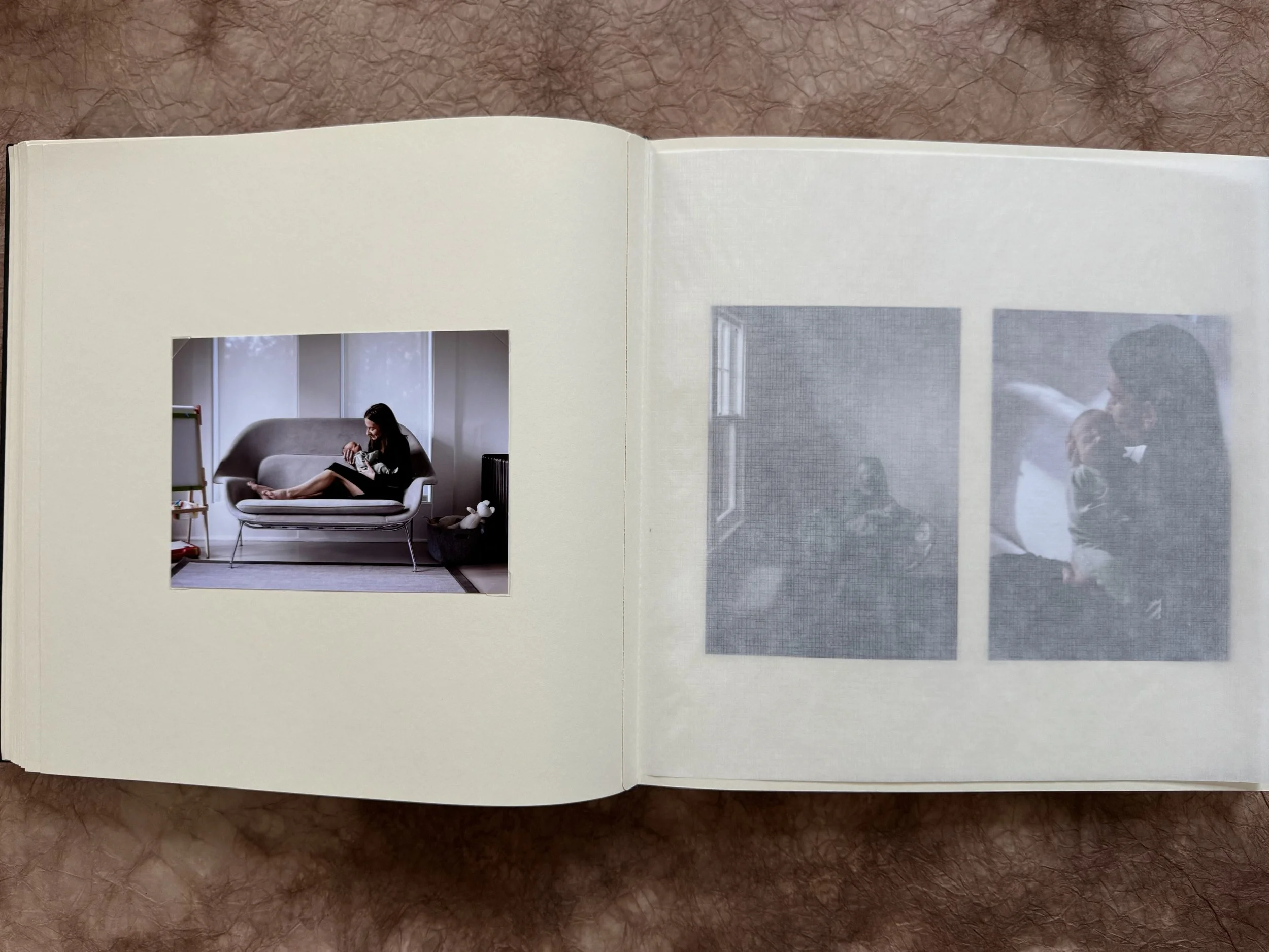 Open photo book showing a color photograph of a woman sitting on a modern sofa with a tablet, in a bright, minimal room. Opposite page shows two grayscale images of a person in a dark room with windows.