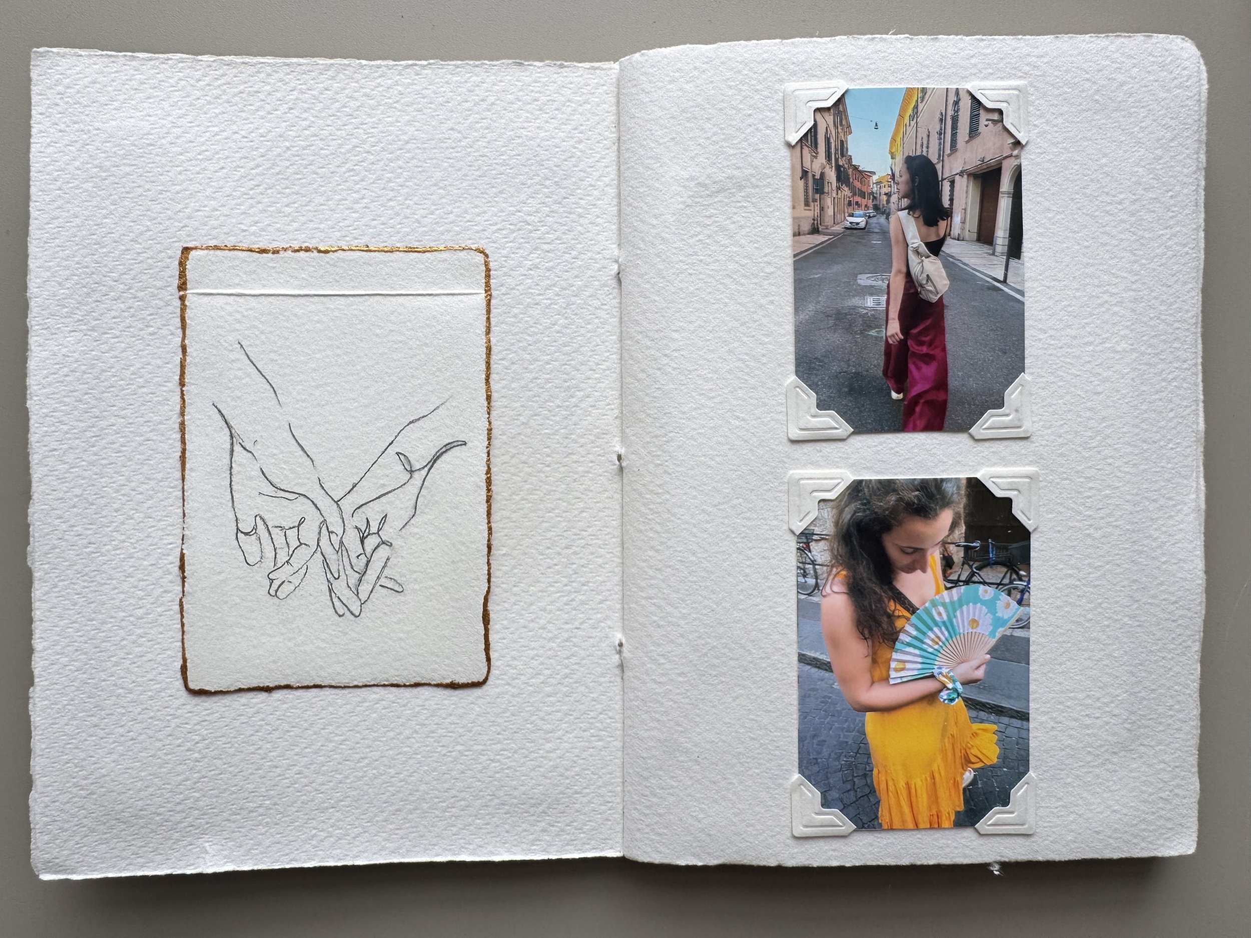 Open photo album showing two portraits of women on city streets, one looking away and the other holding a fan, with a sketch of two hands holding each other on the left page.