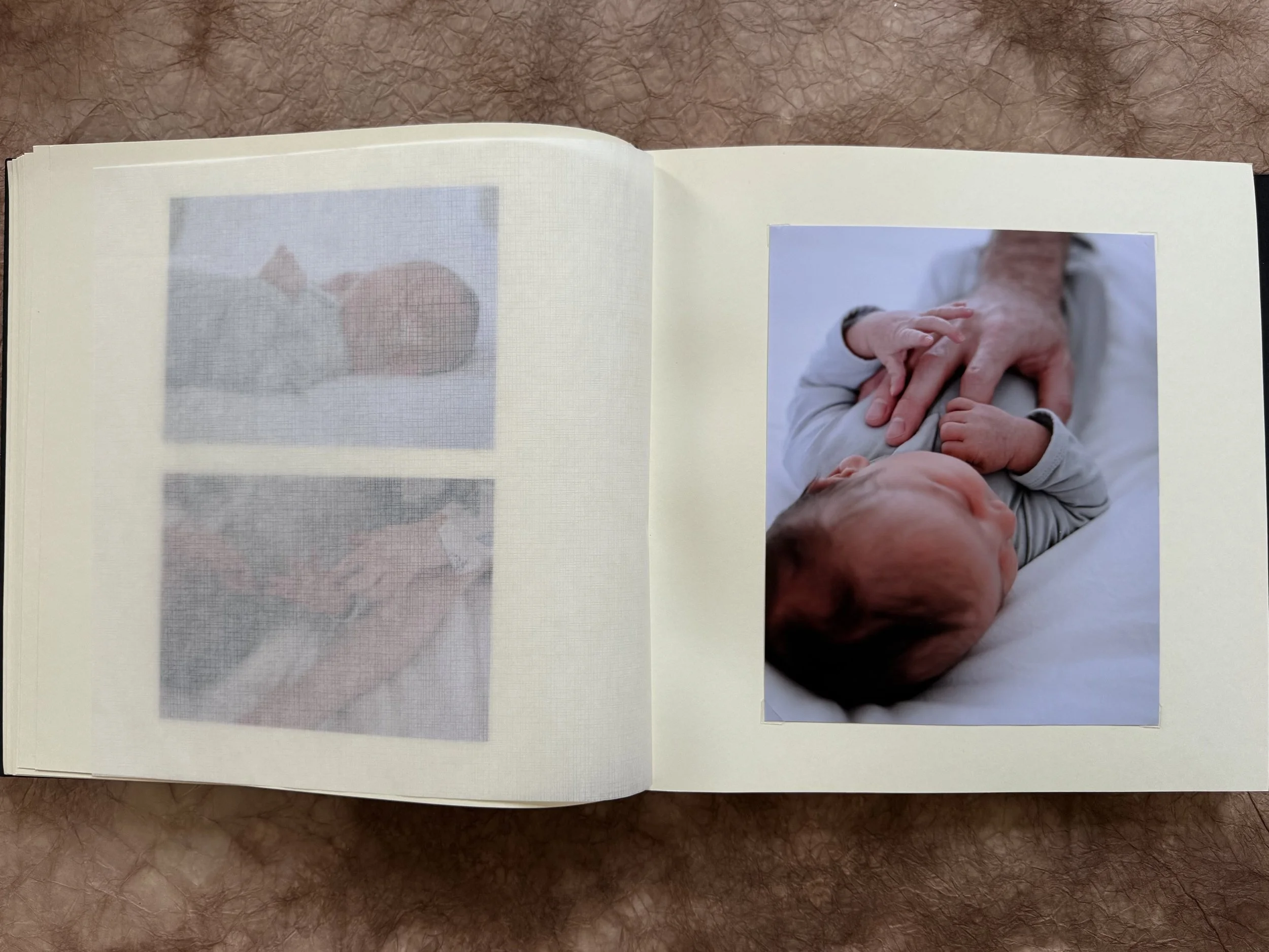 Open photo album showing a photo of a baby lying down and holding an adult's hand on the right page.