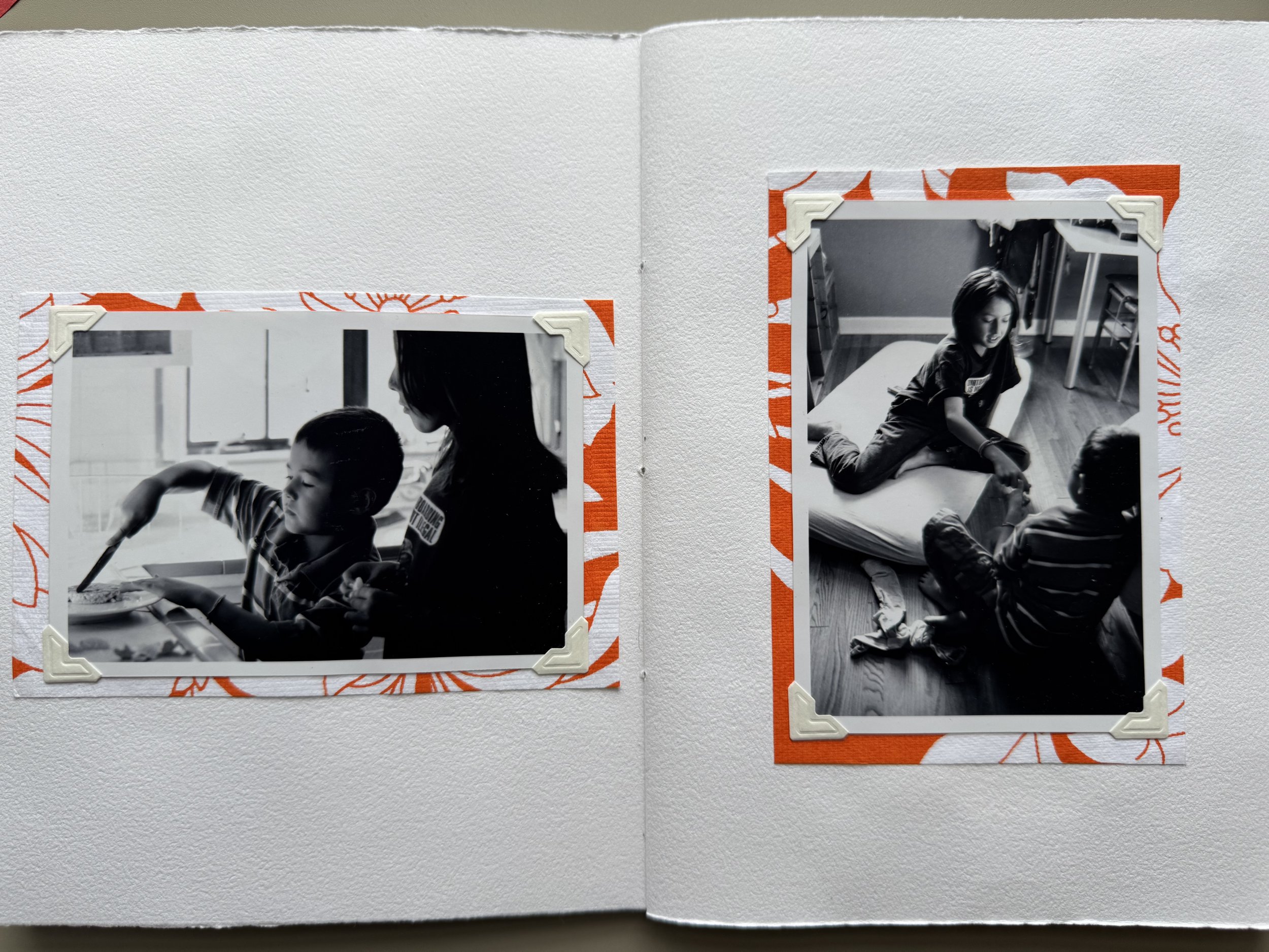 Two black and white photos of children, one on each page of a photo album, with orange and white floral-patterned background and corner protectors.