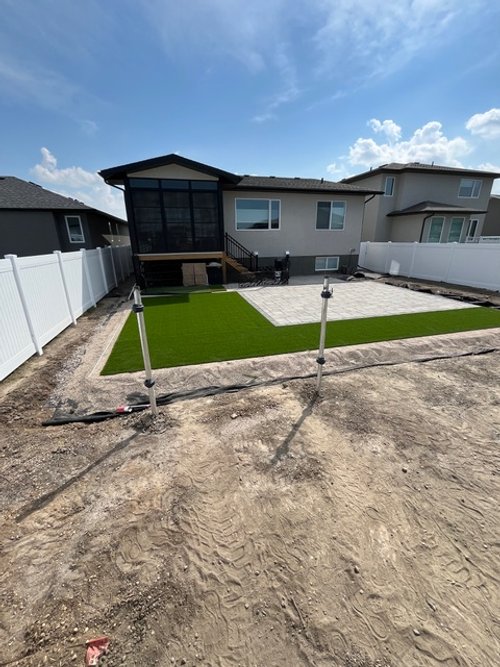 Backyard with artificial grass, paver patio, white fence, and newly installed outdoor lights.