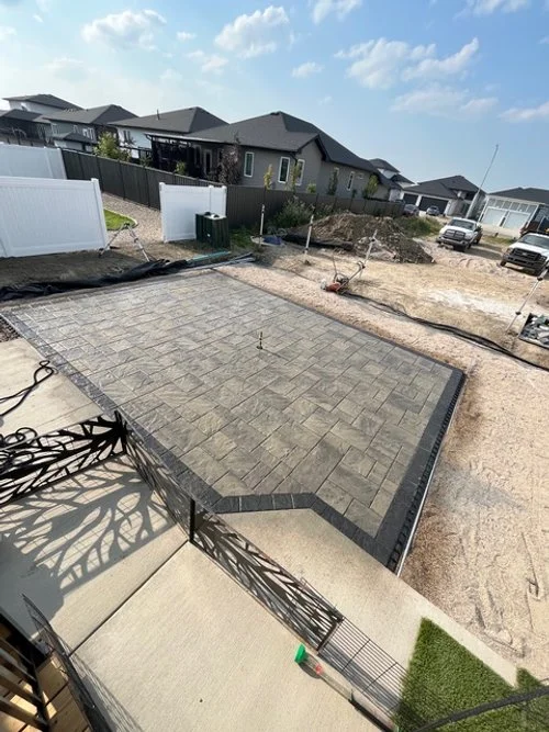 Newly paved backyard patio with interlocking stone design, surrounded by construction area and neighboring houses.