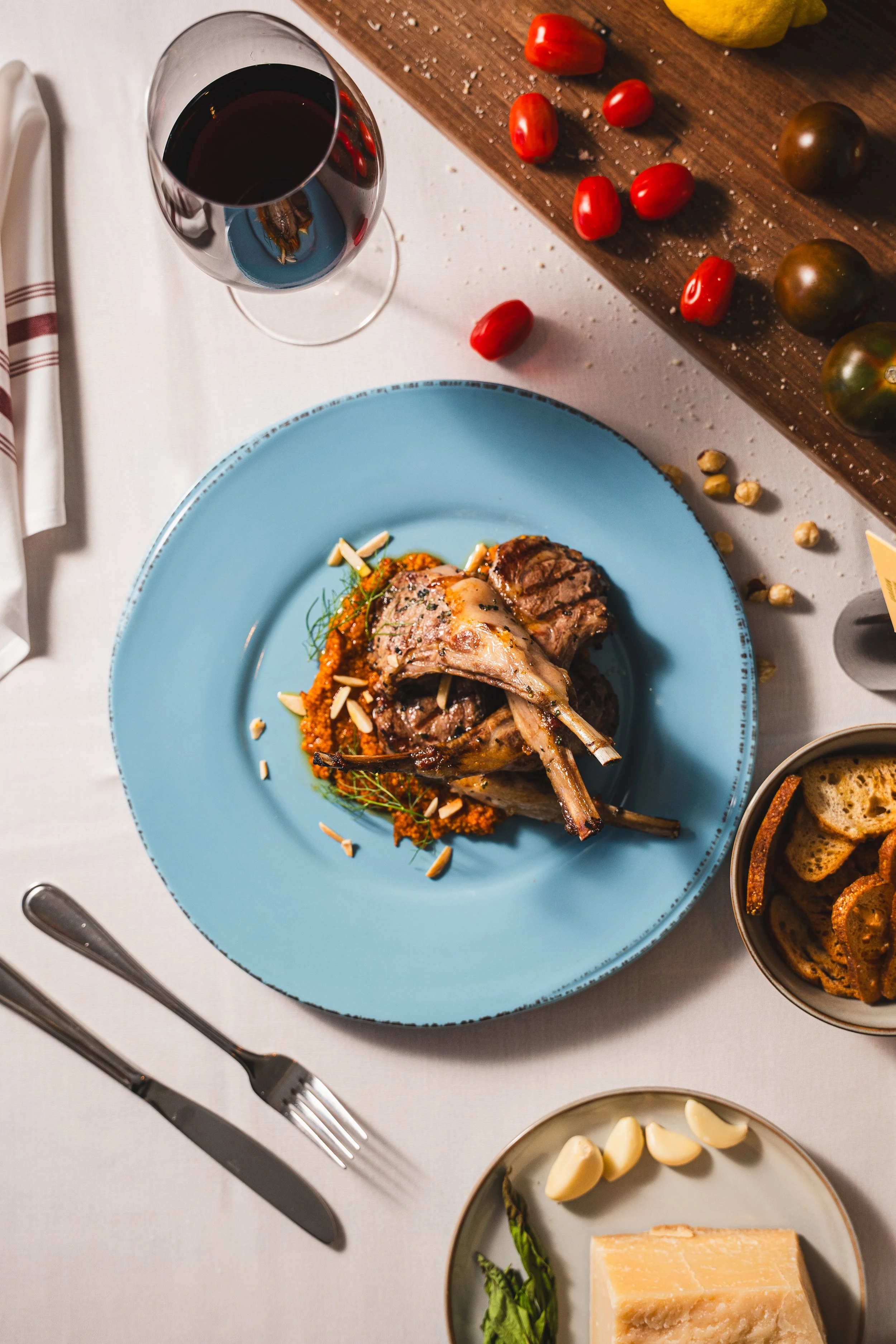 A dinner plate with cooked lamb chops on a bed of orange-colored vegetables, garnished with sliced almonds, on a light blue plate.