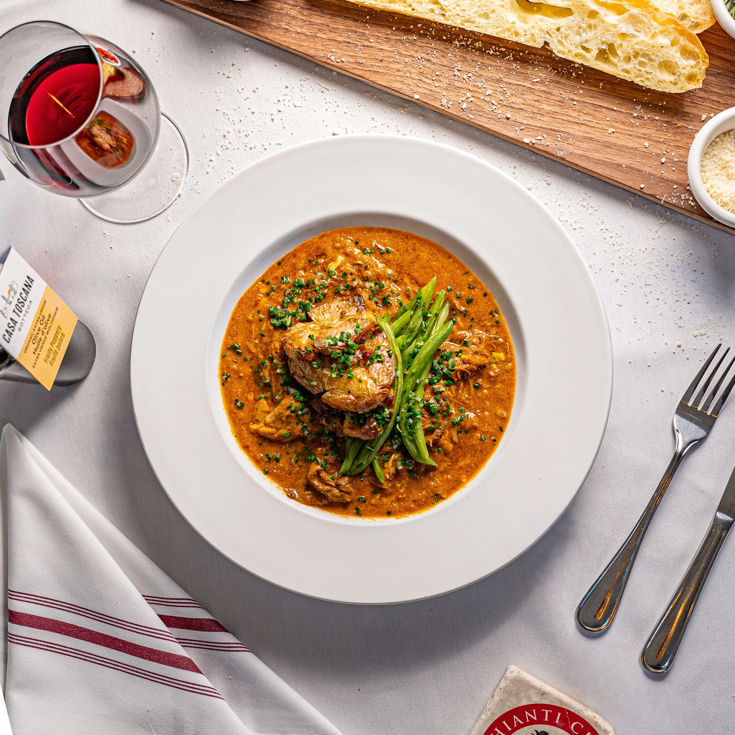 A plate of chicken and green beans in a creamy, orange-colored sauce, garnished with chopped herbs on a white tablecloth.