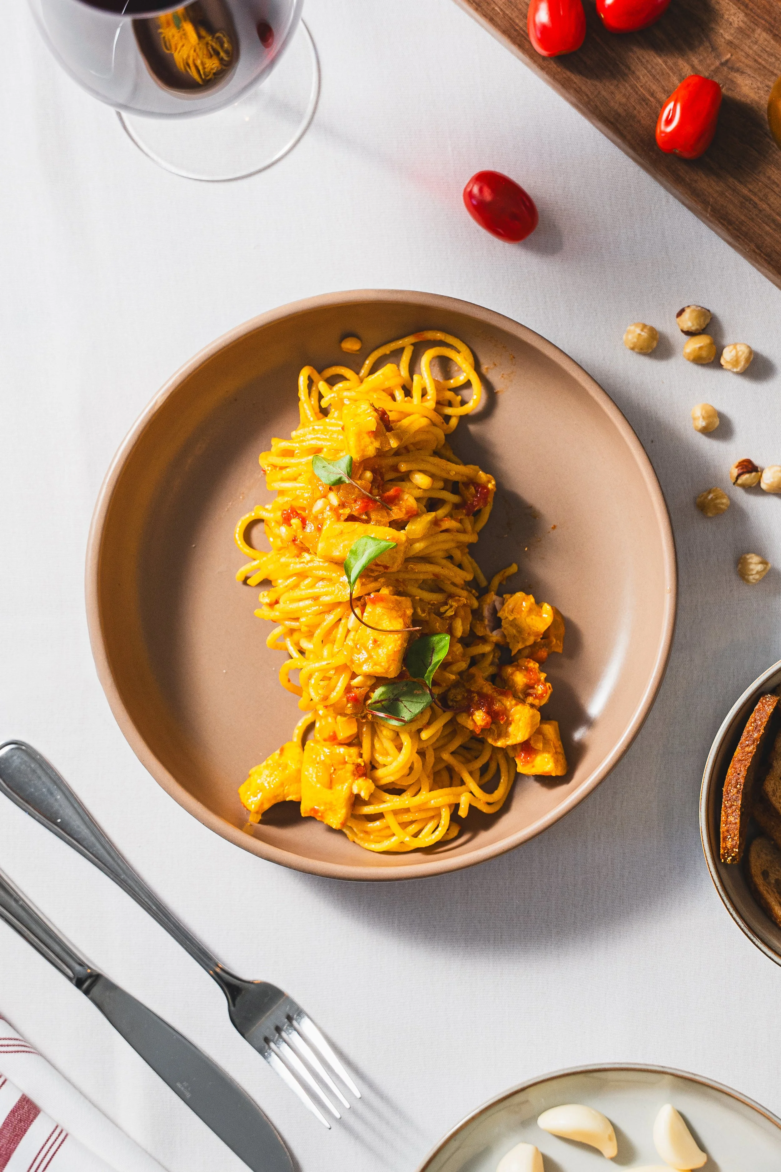 A plate of spaghetti with chicken and tomato sauce garnished with basil leaves on a white tablecloth.