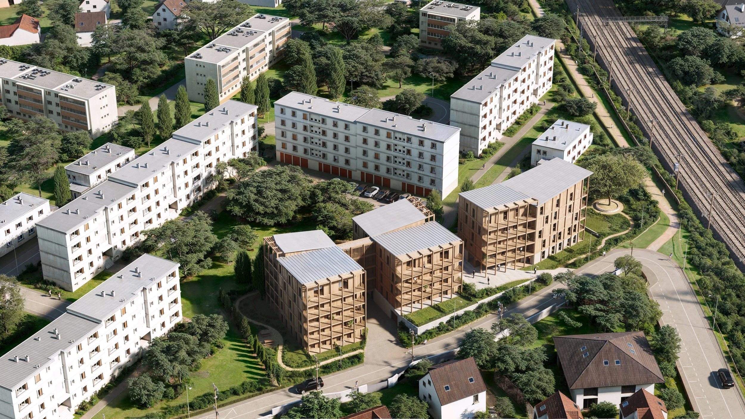 Vista aérea de un complejo residencial con edificios de diferentes tamaños y estilos, rodeados de áreas verdes, caminos y árboles, cerca de vías de ferrocarril.