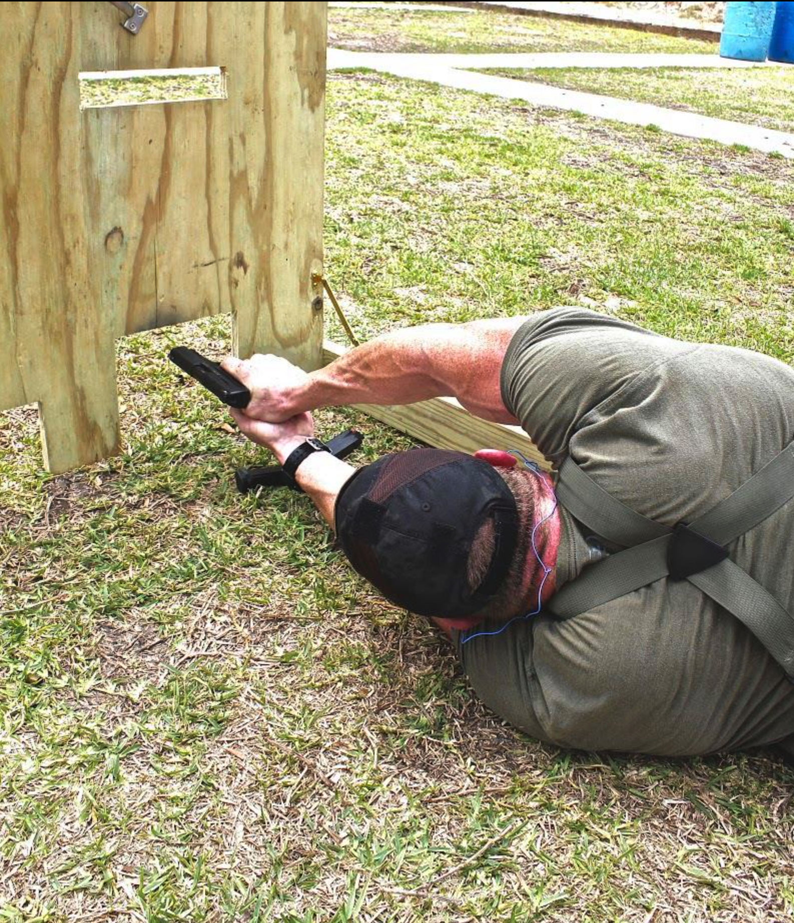 A man kneeling on the ground using a drill to screw into a wooden structure outdoors.