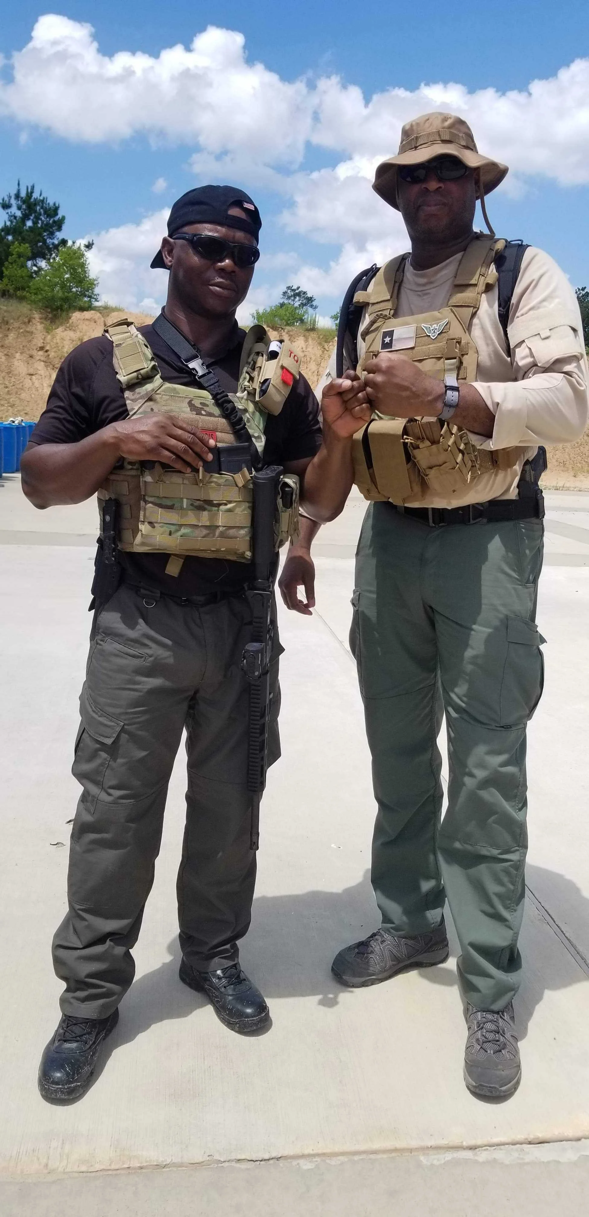 Two men in military or tactical gear standing outdoors on a sunny day, fist bumping.