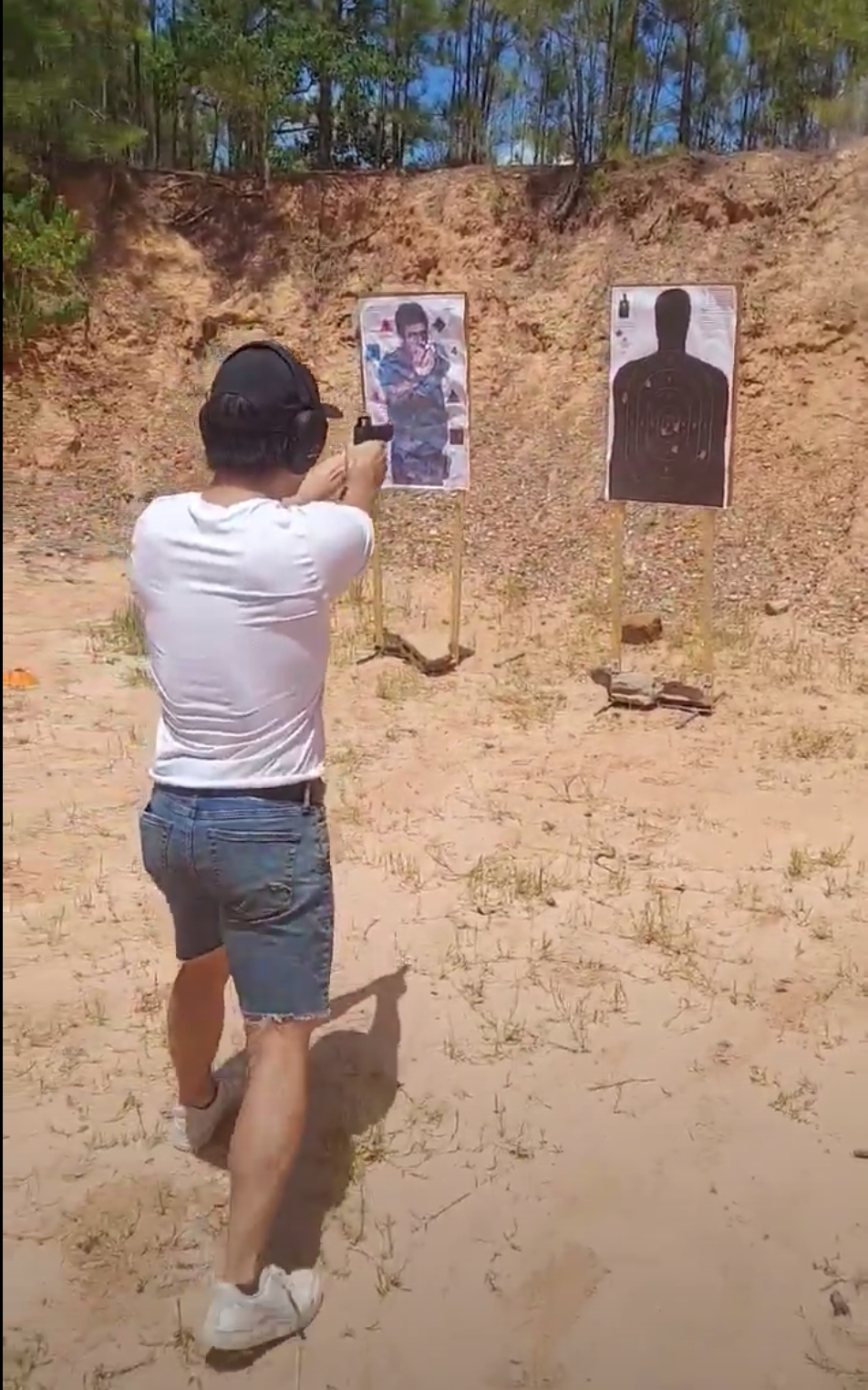 Man shooting at targets on outdoor shooting range, with silhouette targets and a picture of a person in military uniform.