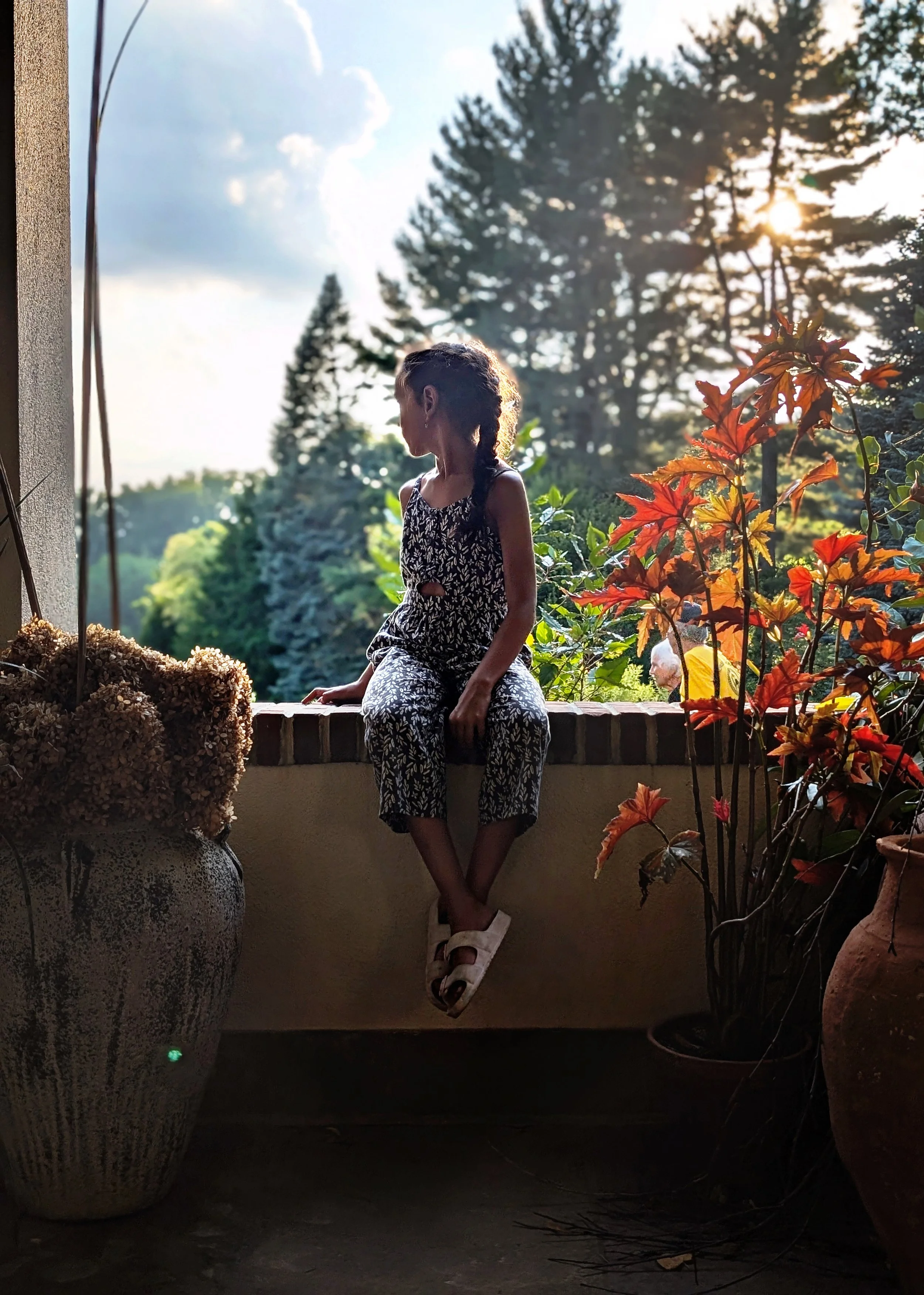 a girl sits on a ledge with her face turned away from the camera. Fall leaves