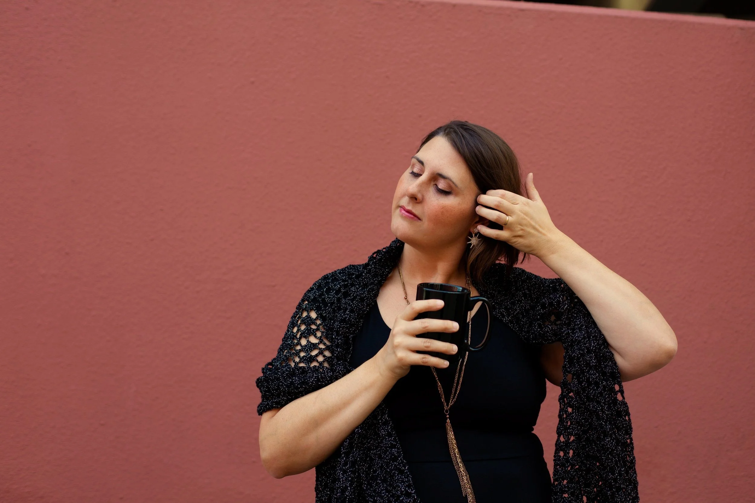 Sylvia Mallory is the founder and owner of Crone House. She is wearing a black dress and shawl in front of a dusty pink wall.