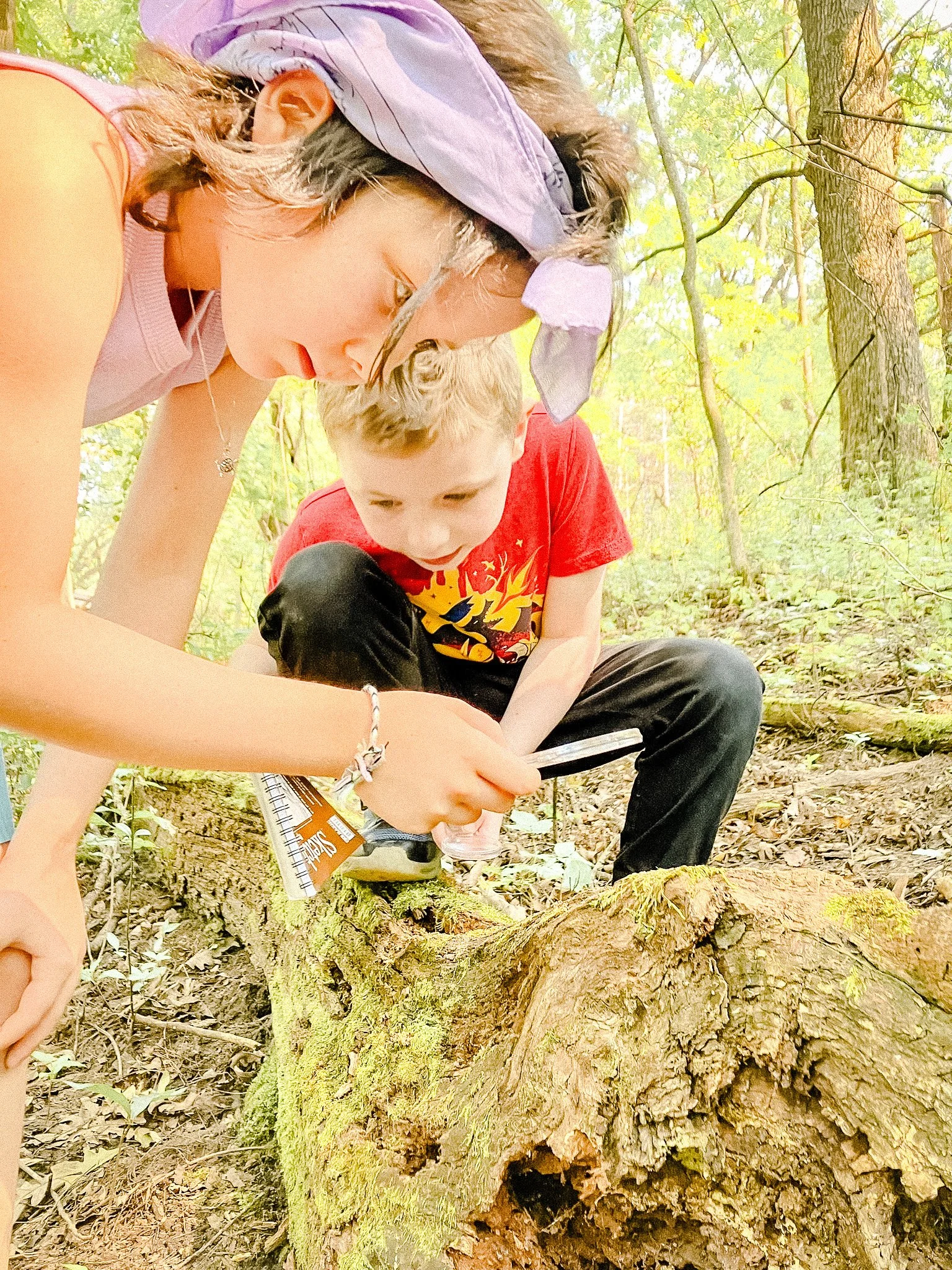 Elementary students examine a mossy log with a magnifying glass, demonstrating River Grove’s hands-on environmental education and place-based science curriculum.