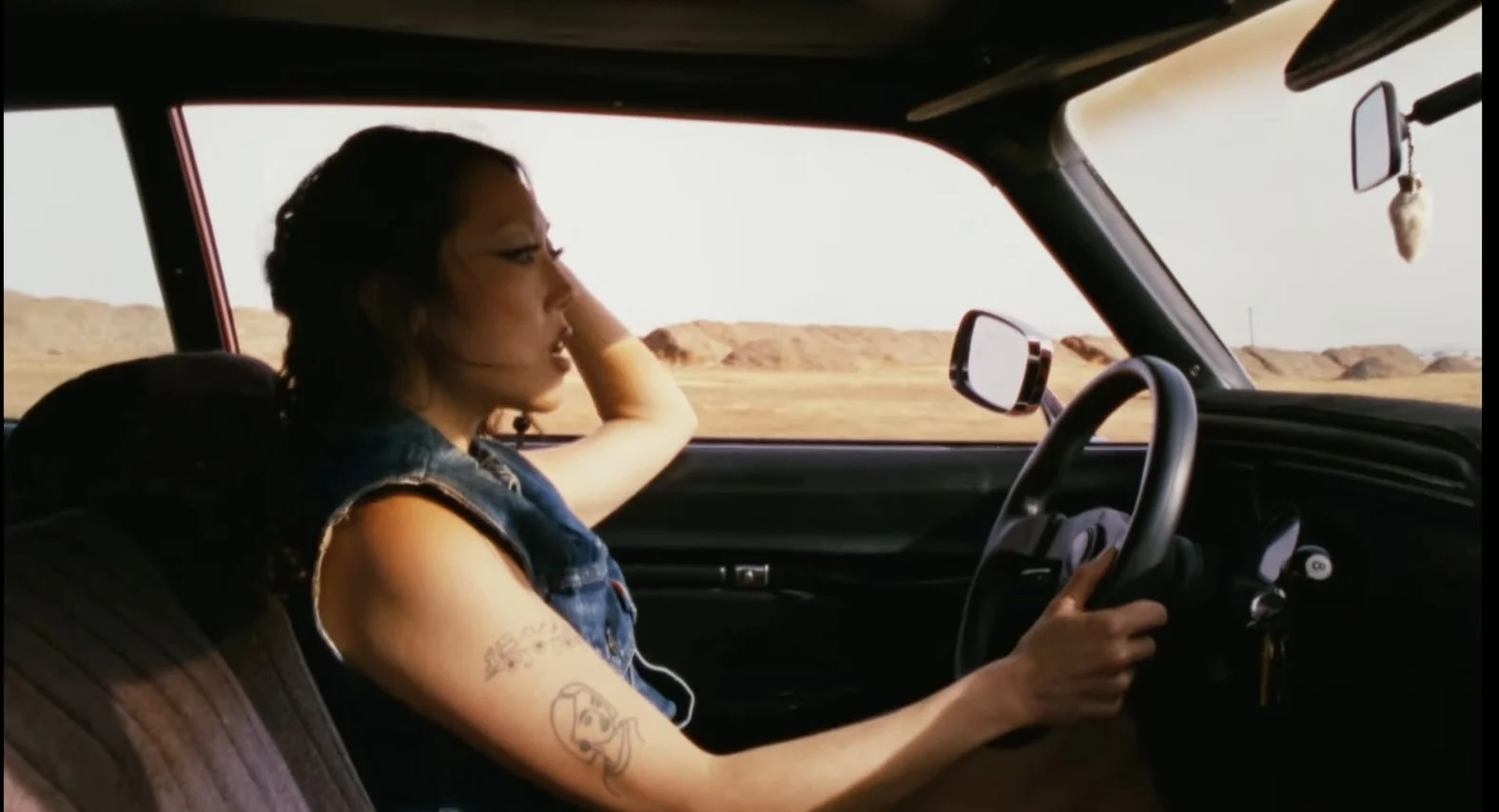A woman with tattoos driving a vehicle through a desert landscape
