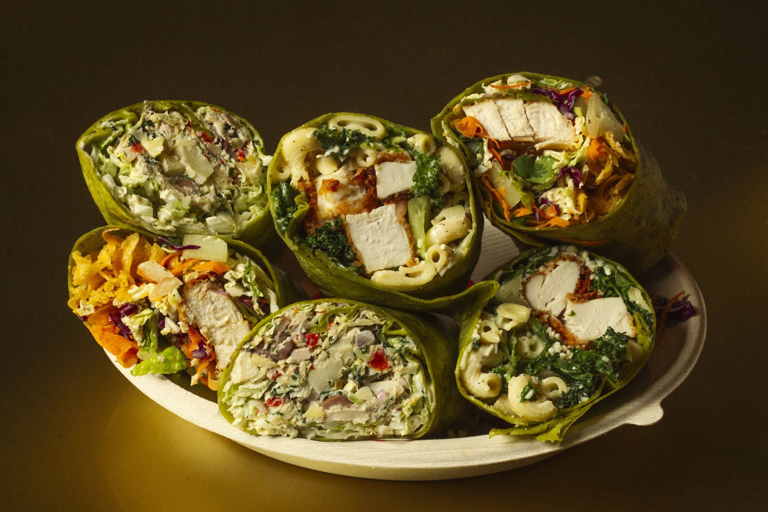 Various sushi rolls with vegetables and chicken, arranged on a white plate against a dark background.