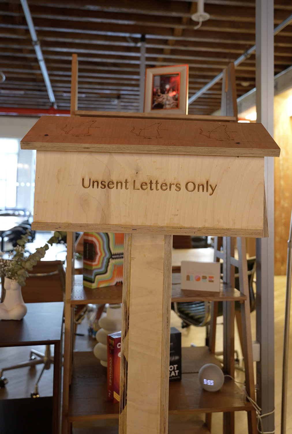 Wooden sign reading 'Unsent Letters Only' inside a store or gallery with furniture and decorative items in the background.