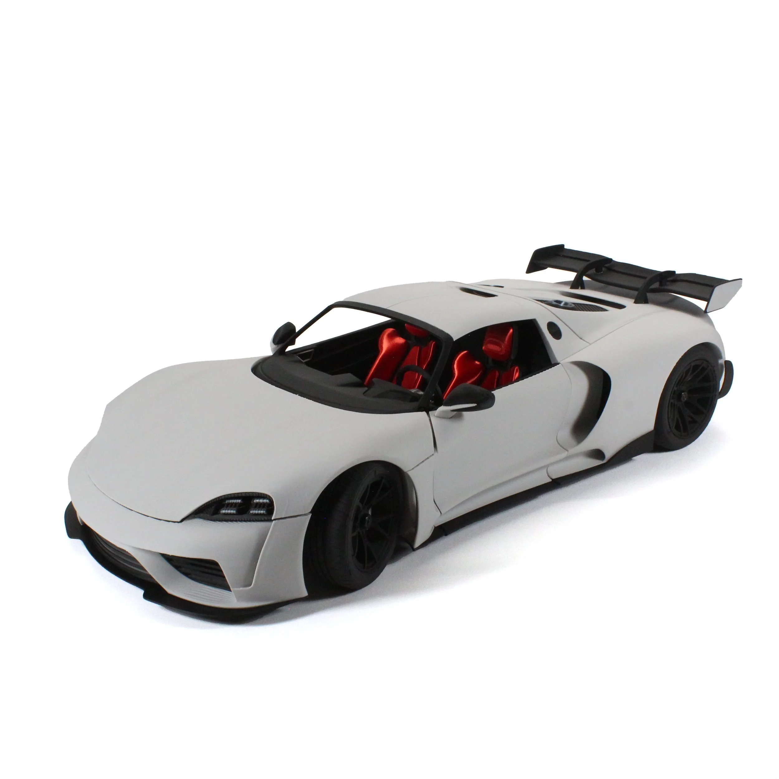 White scale model sports car with red interior, black wheels, and rear wing, isolated on white background.