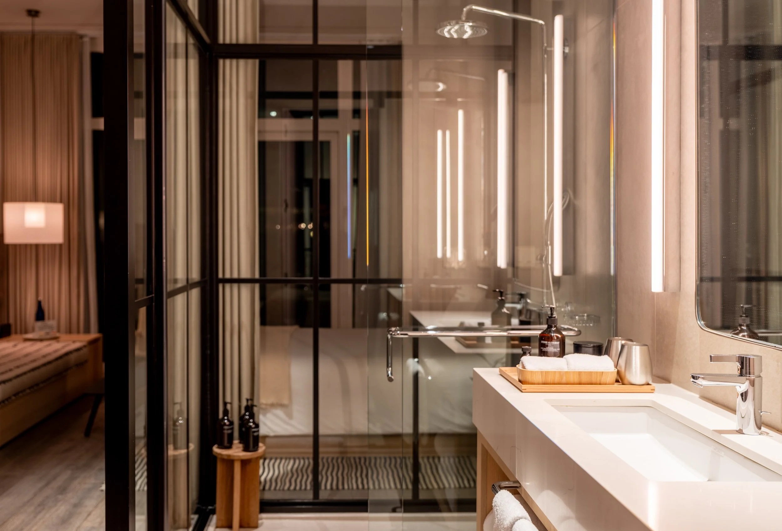 Modern bathroom with a white sink, faucet, mirror, and countertop, illuminated by bright lighting, with storage and towels visible.