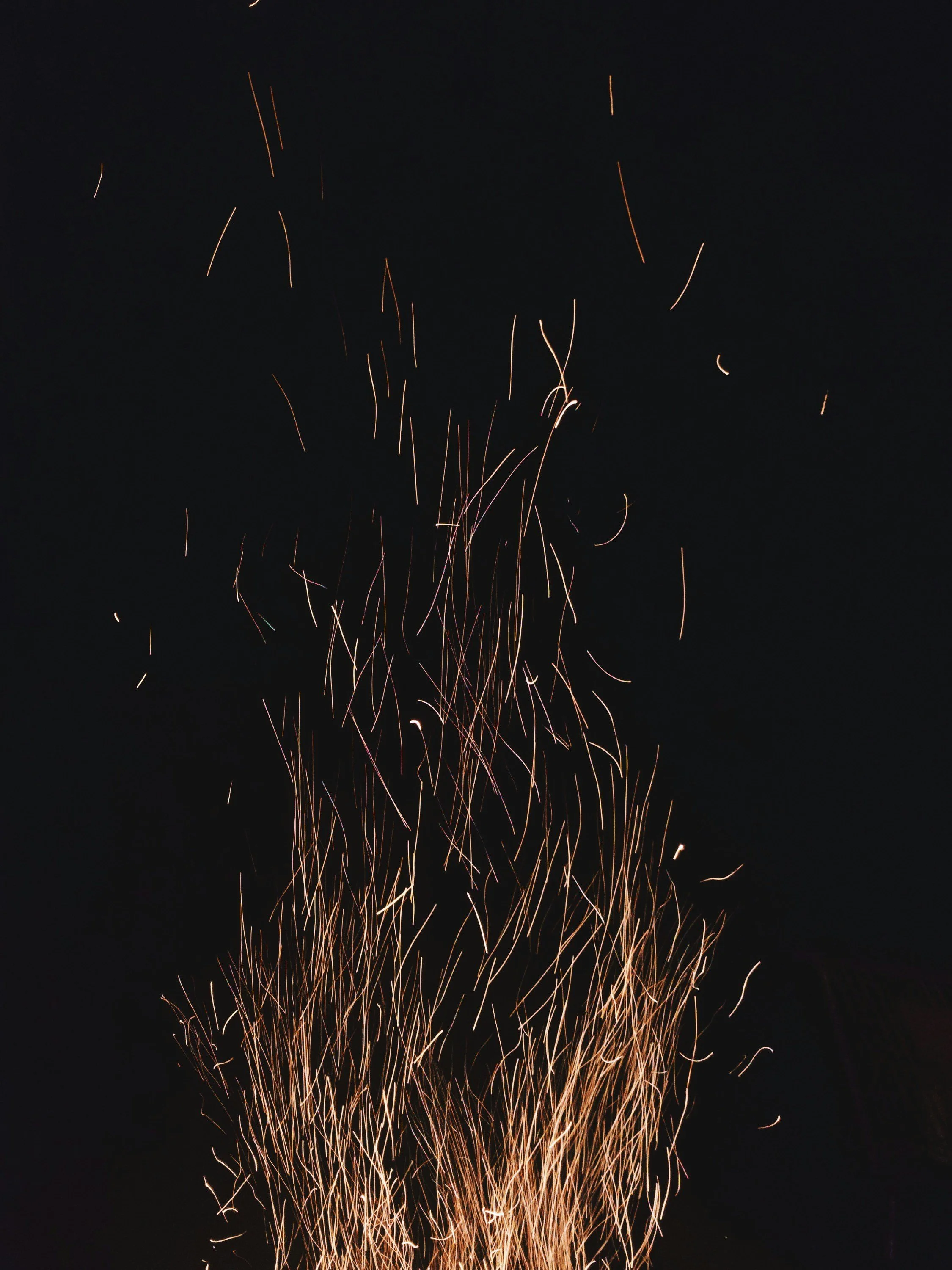 Golden sparks rising into the night sky from a fire, symbolizing inner transformation, devotion, and the slow unfolding of personal healing.