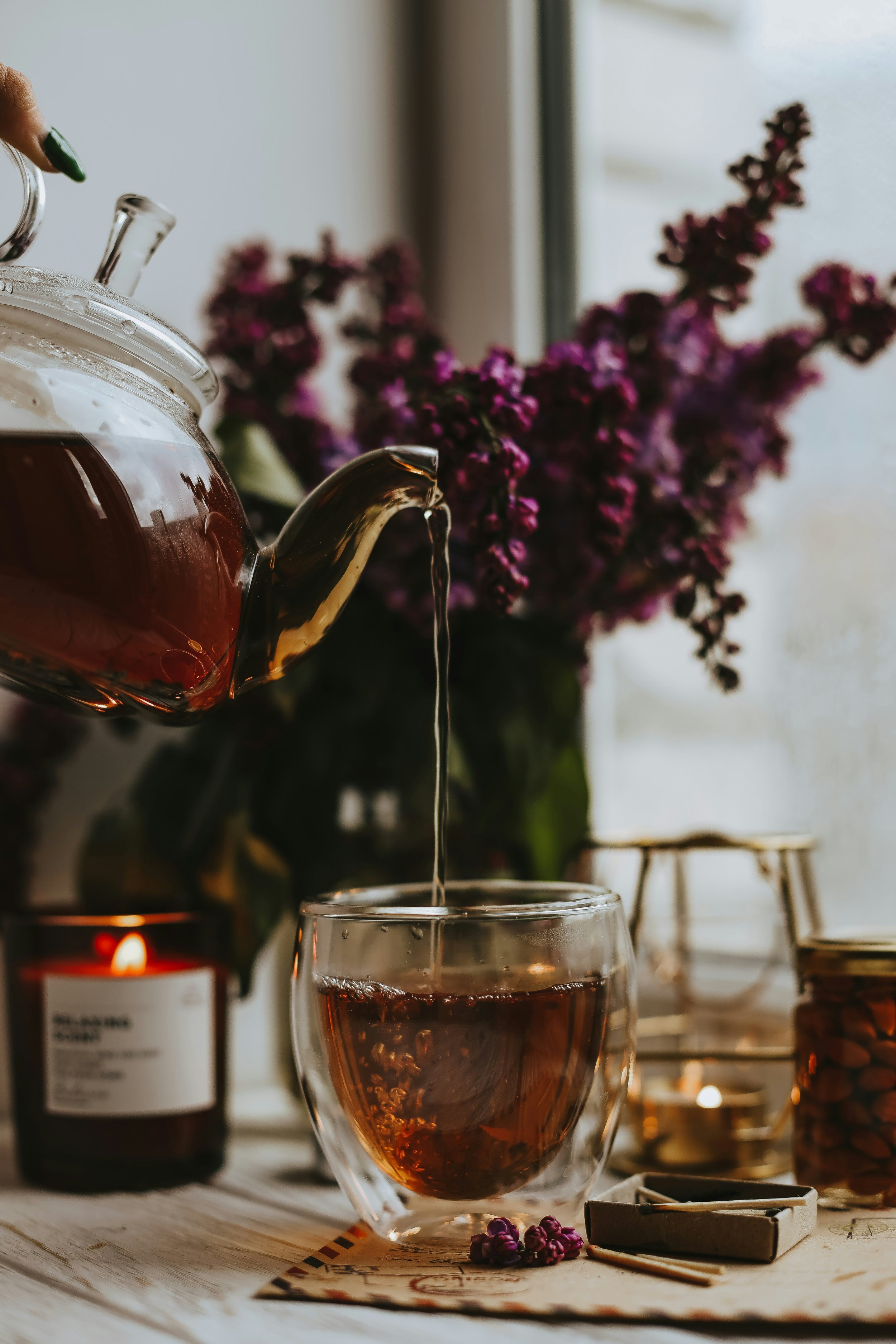 Pouring herbal tea beside candlelight and flowers, symbolizing holistic therapy, ritual, and the integration of body, psyche, and soul.