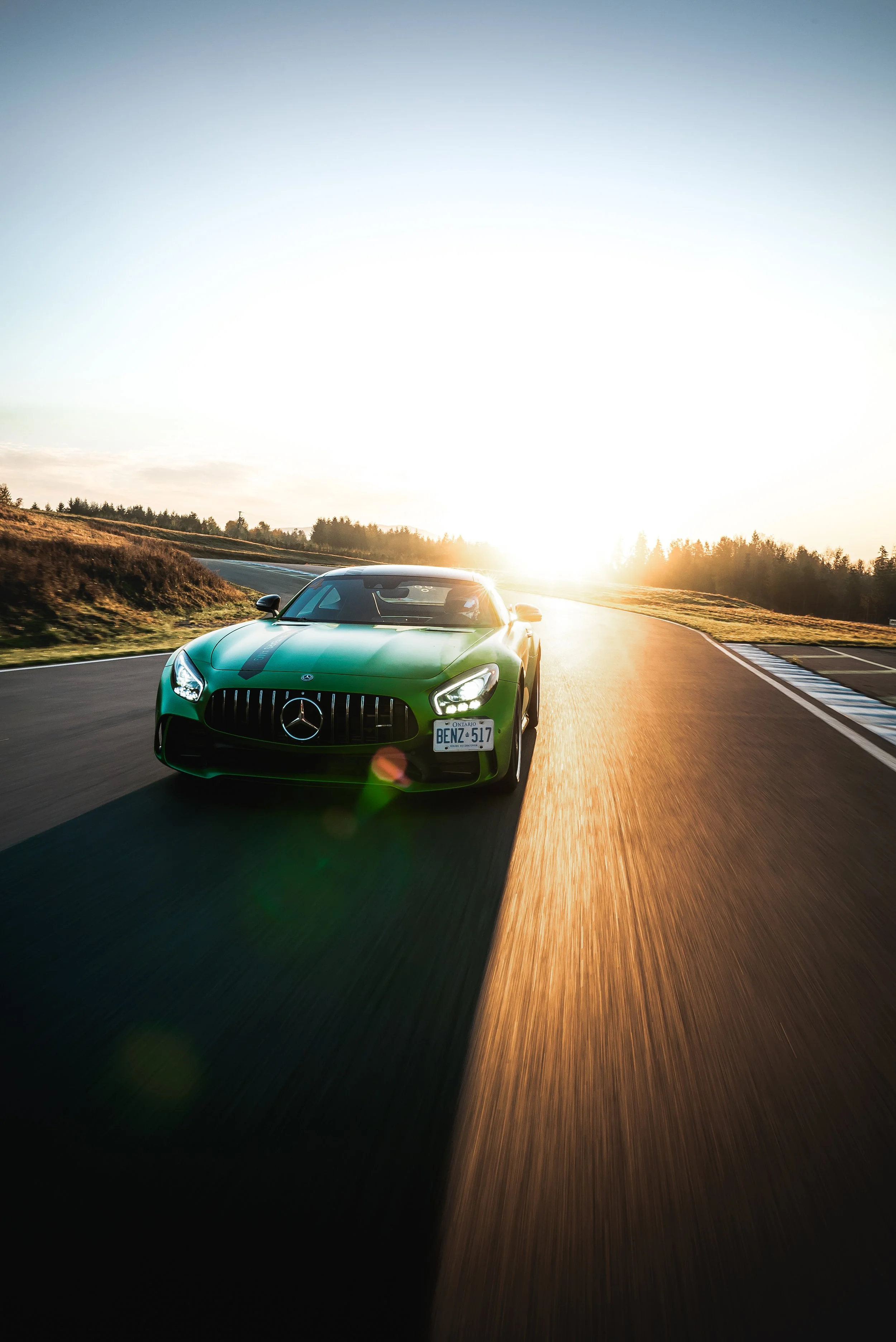 A green Mercedes-Benz sports car driving on a race track at sunset.