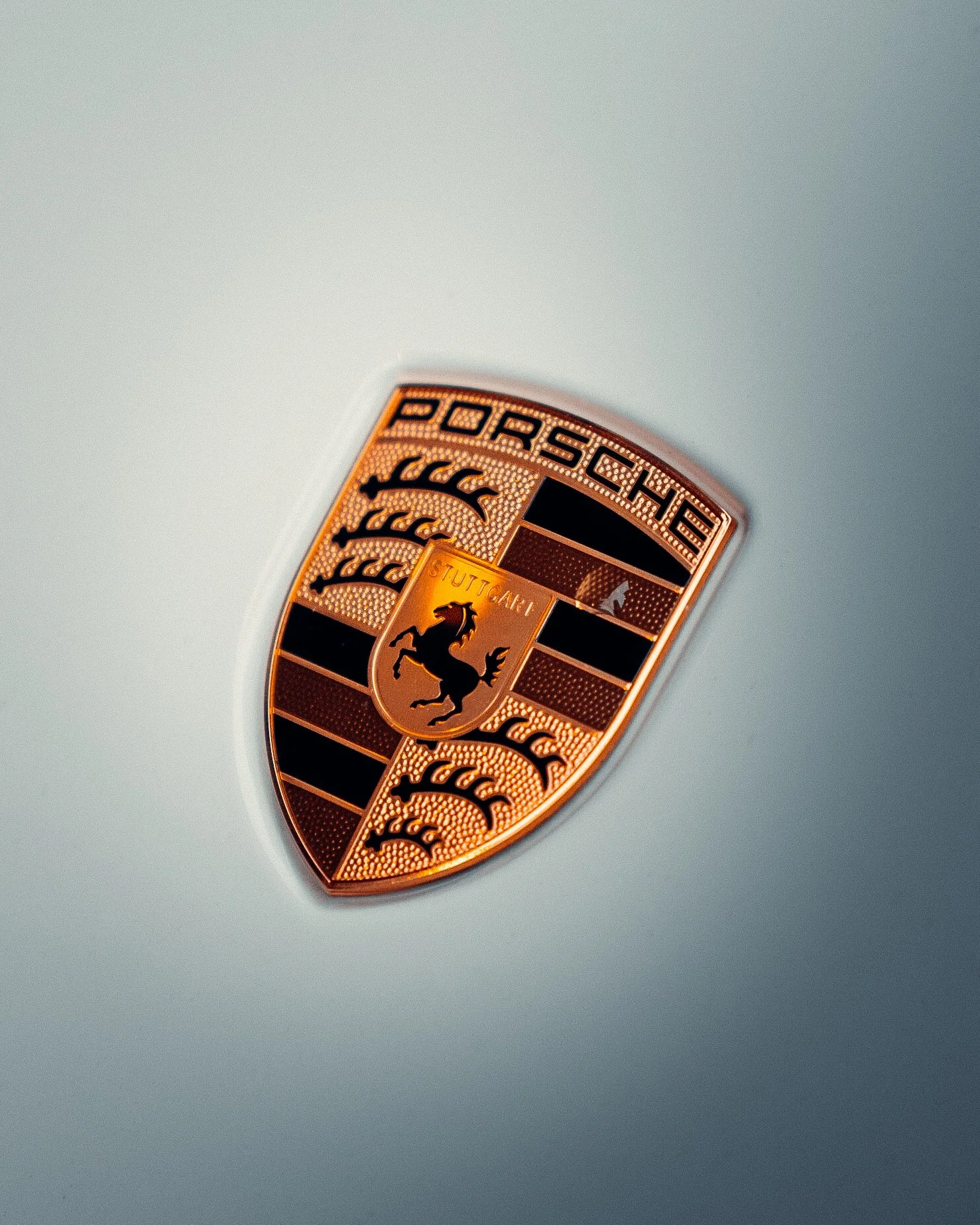 Close-up of a Porsche emblem on a car's hood, featuring a shield with a black horse and the word 'Stuttgart'.