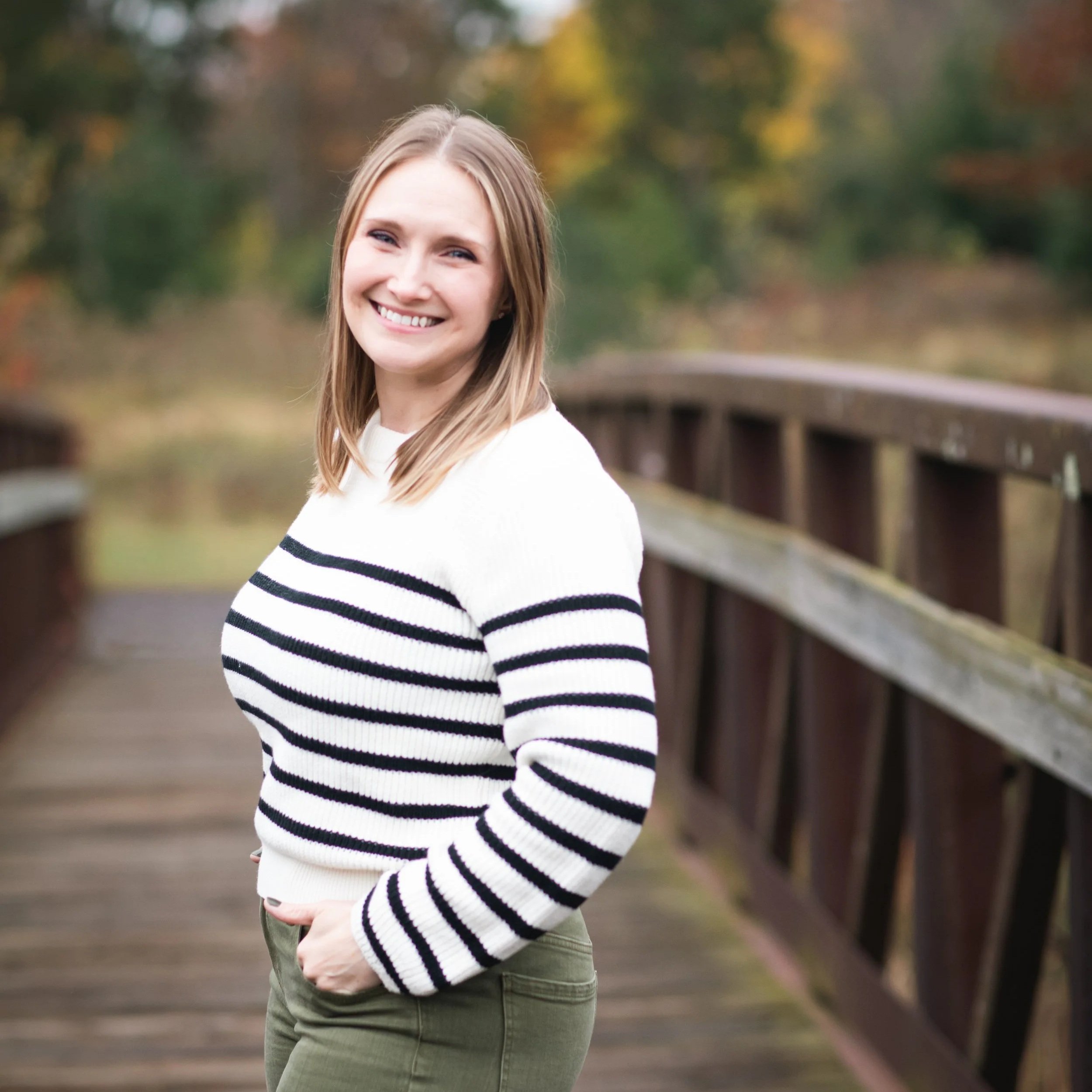 Jennifer Hahn standing on a wooden bridge, white sweater with black stripes. Photo by Sunlit Photography, 2025.