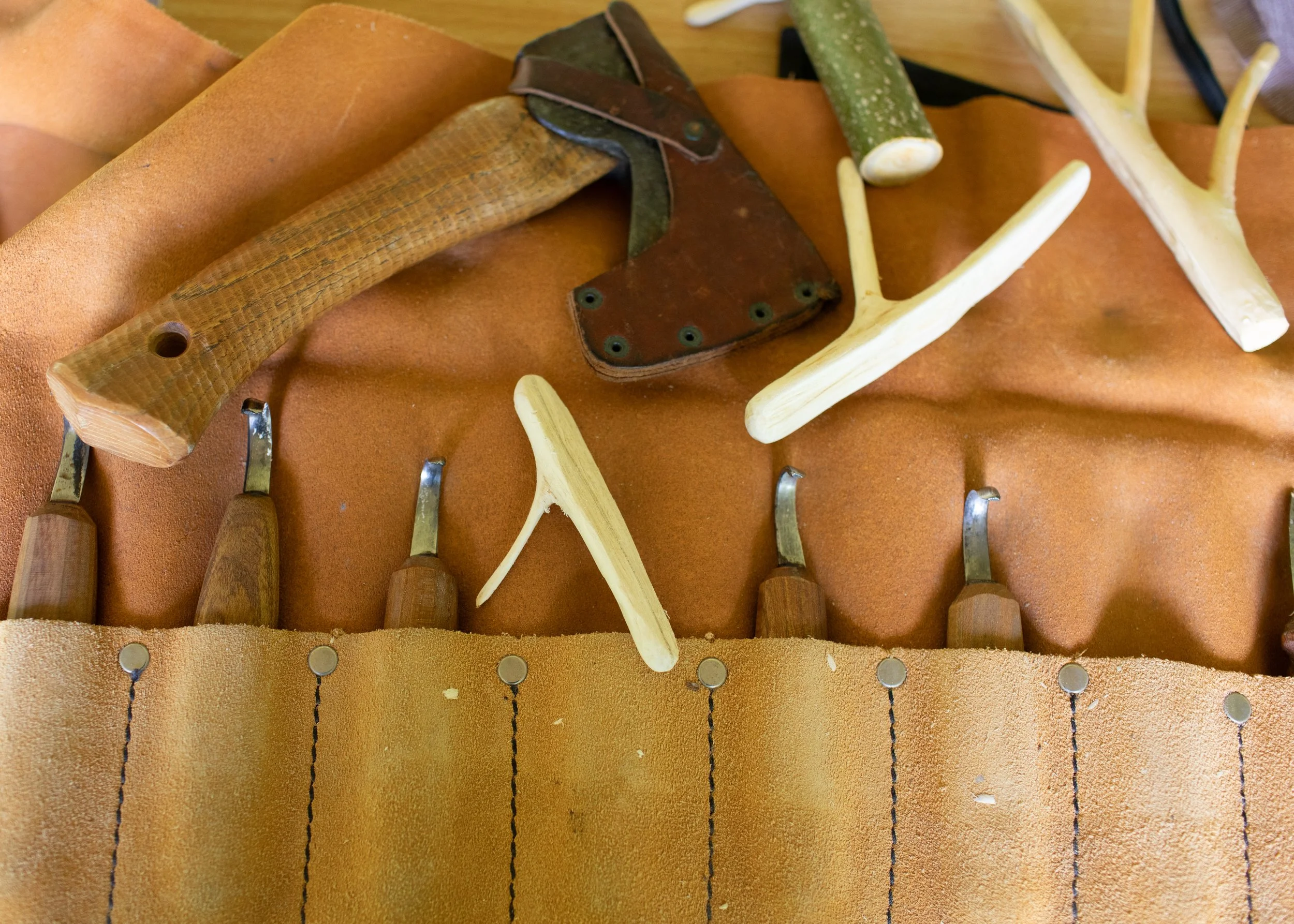 Various woodworking tools including chisels, knives, and antler handles laid on a leather work surface.