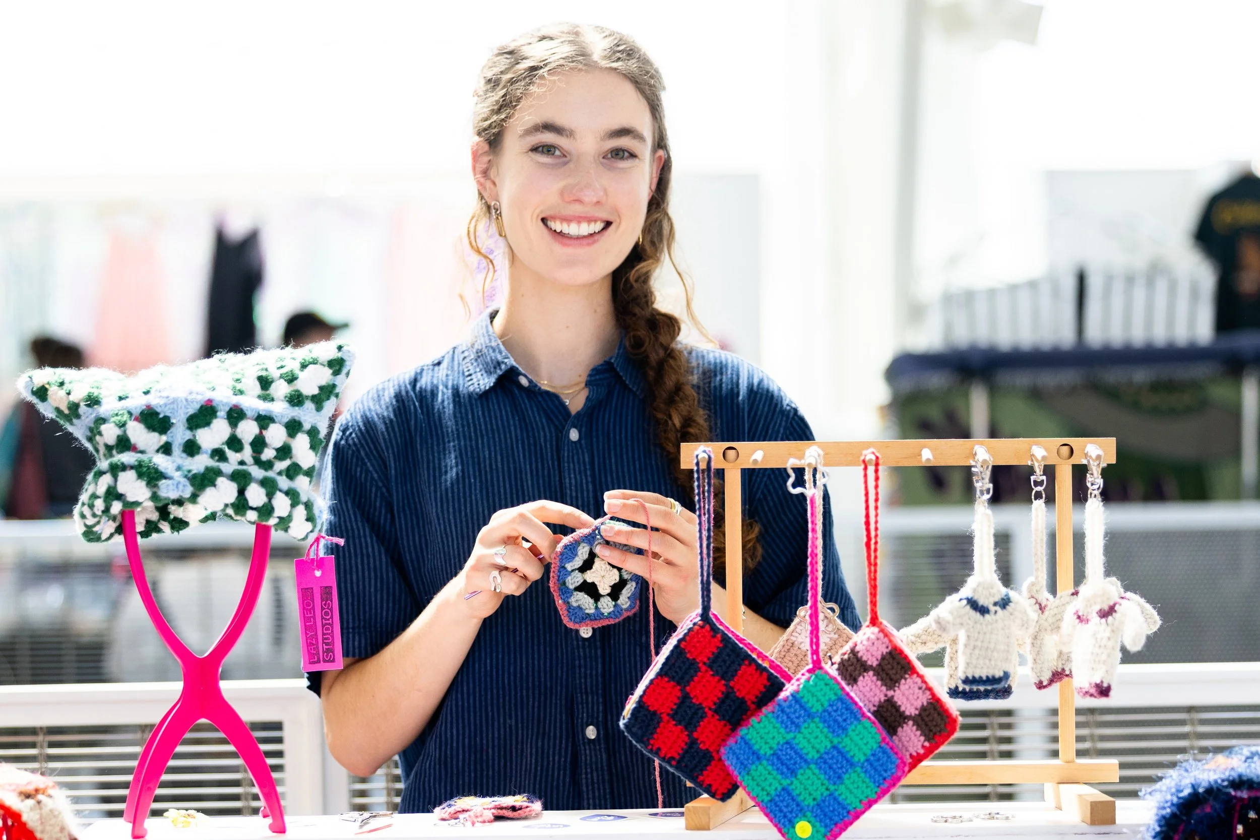 Woman smiling and crocheting behind a display of textiles.