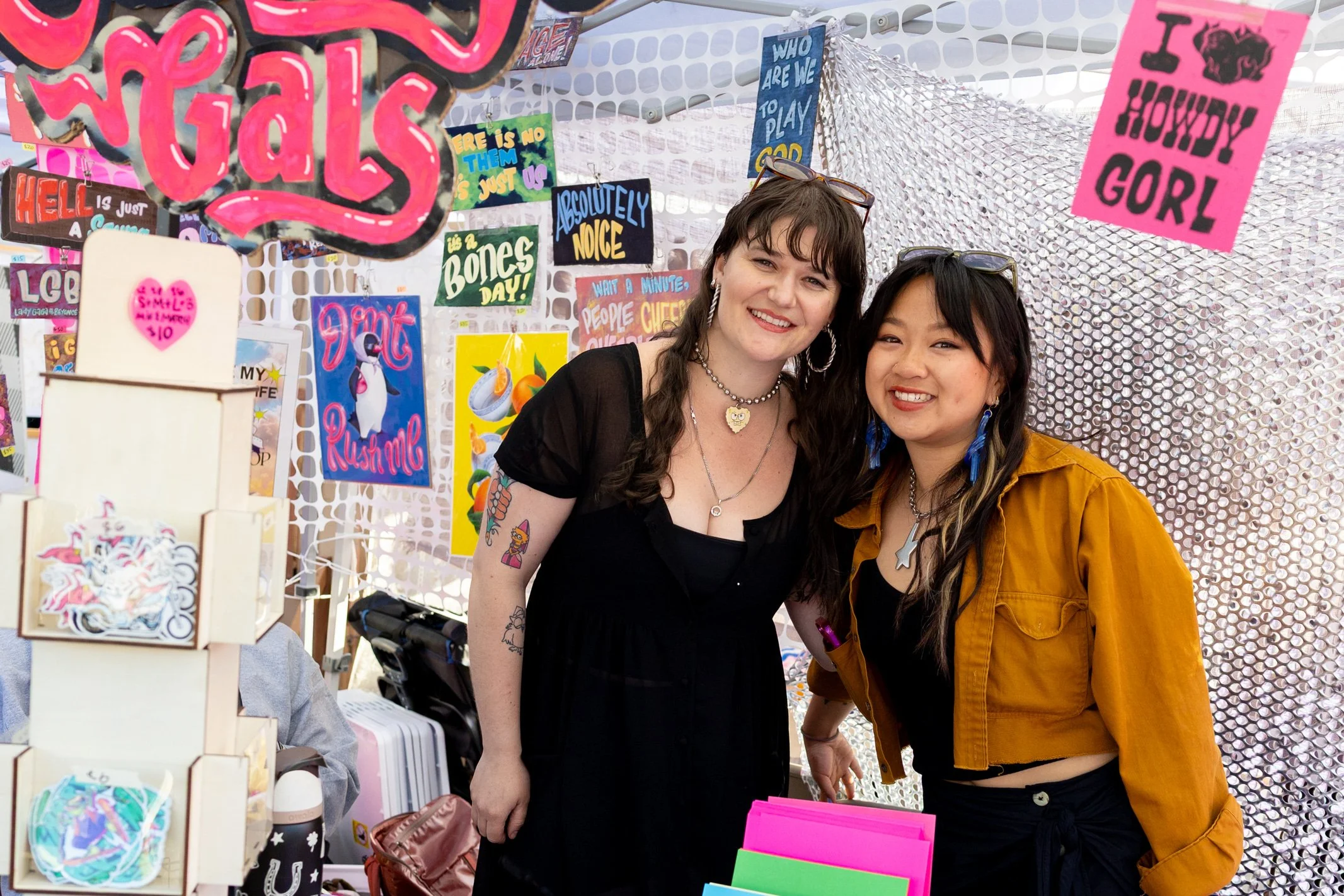 Two women smiling and posing in a booth with various printed matter on display.