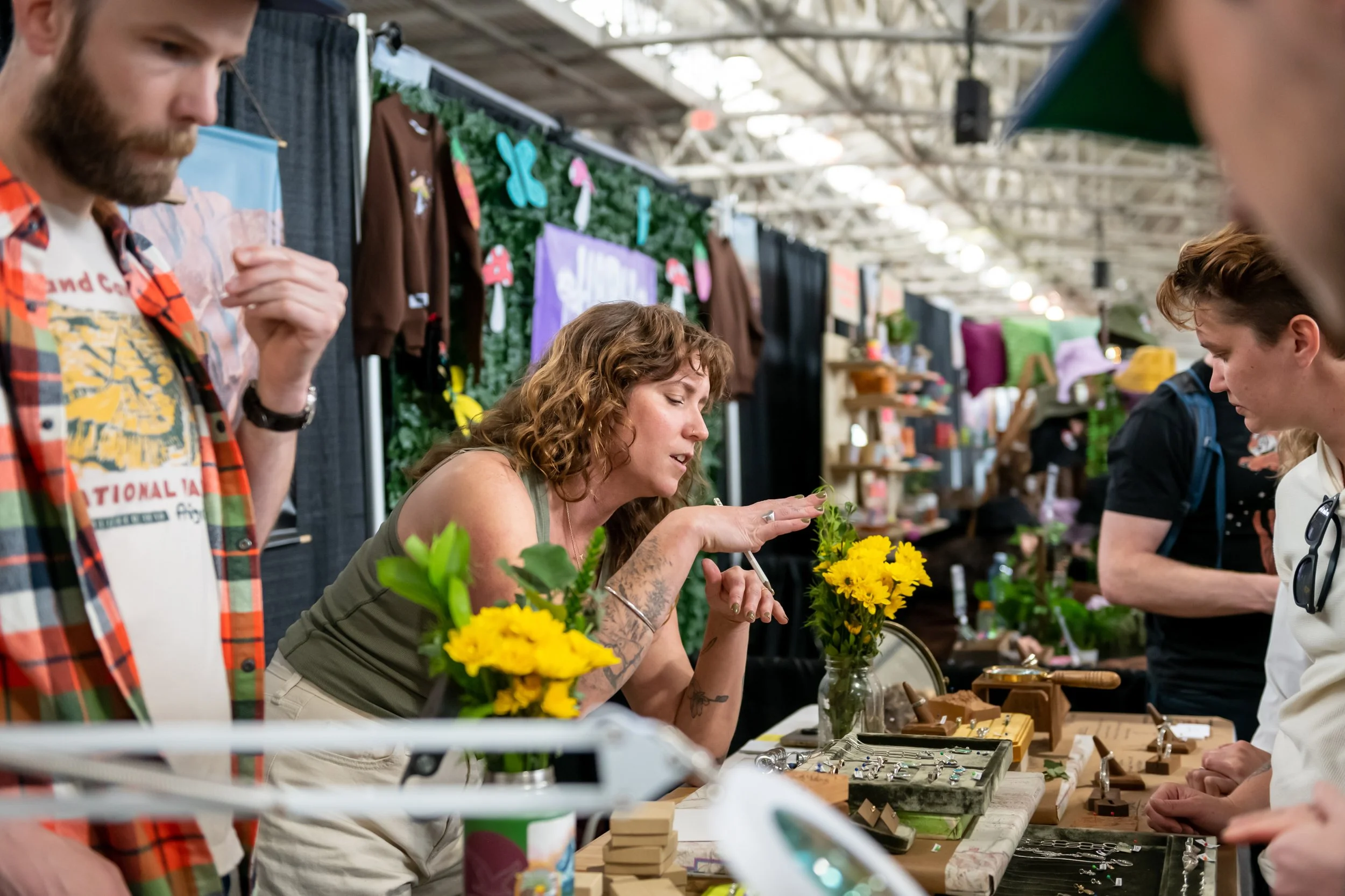 Woman chatting with market-goer at her jewelry display booth.