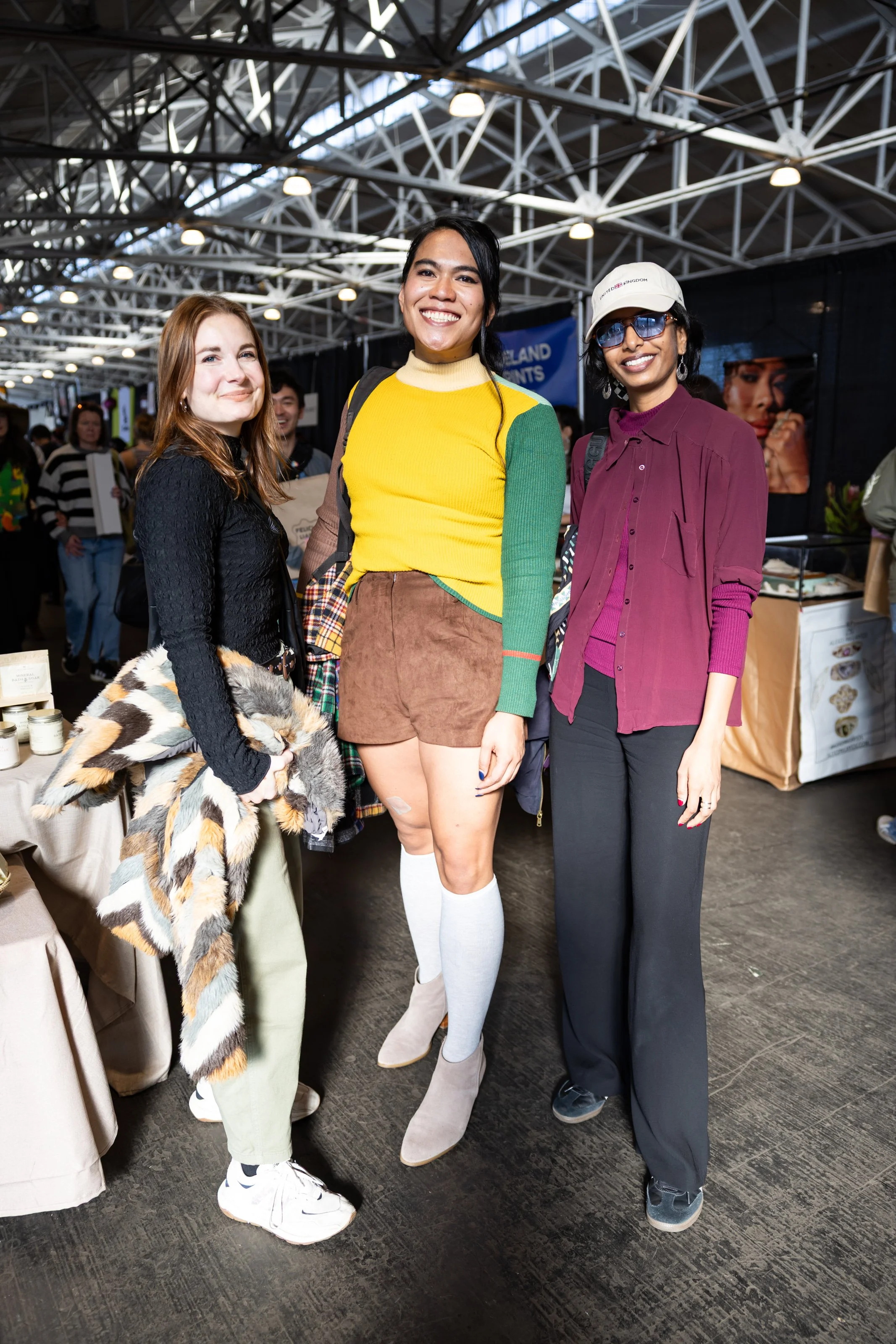 Three friends smiling and posing at an indoor craft show.