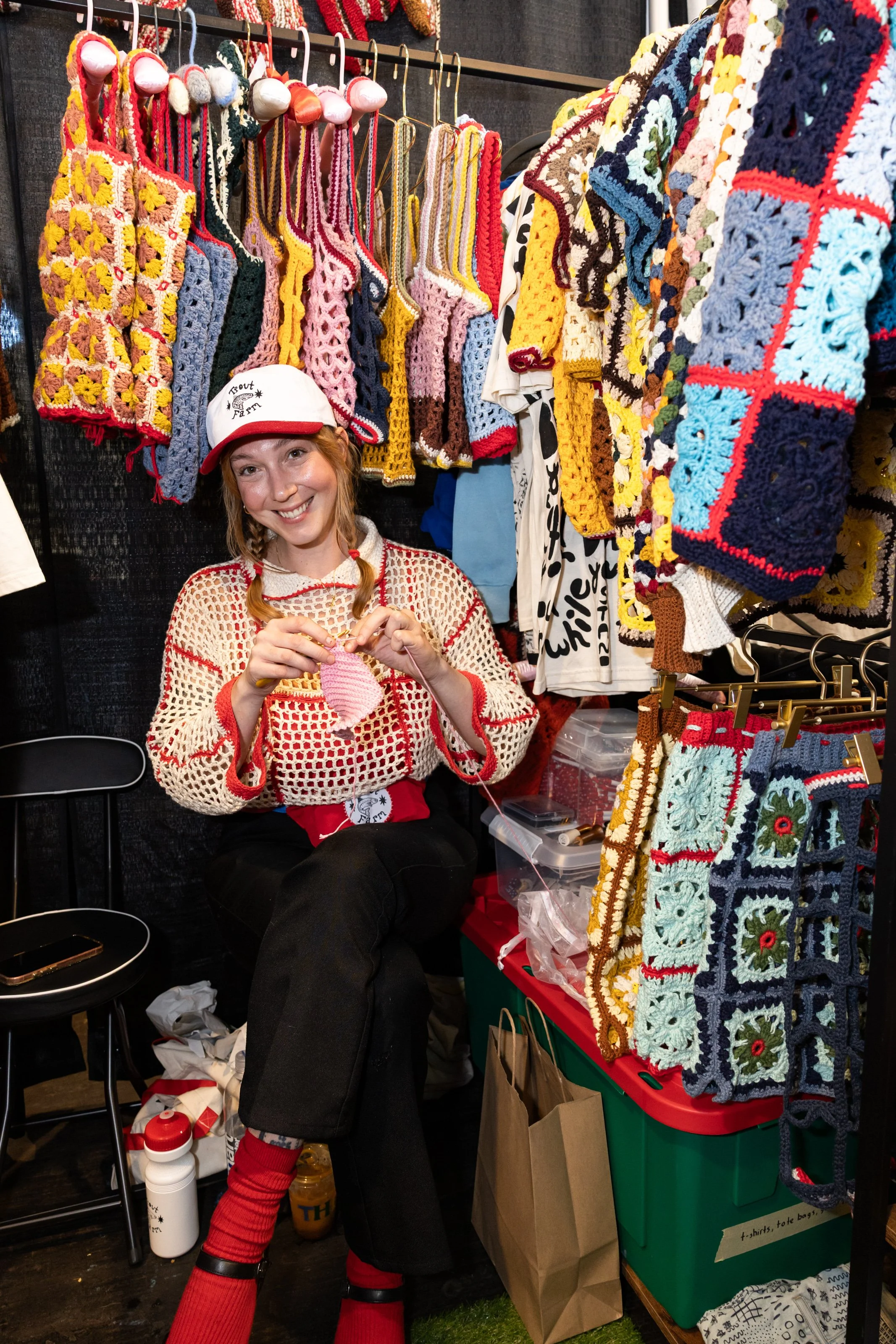 Woman smiling in a booth full of crocheted clothing.