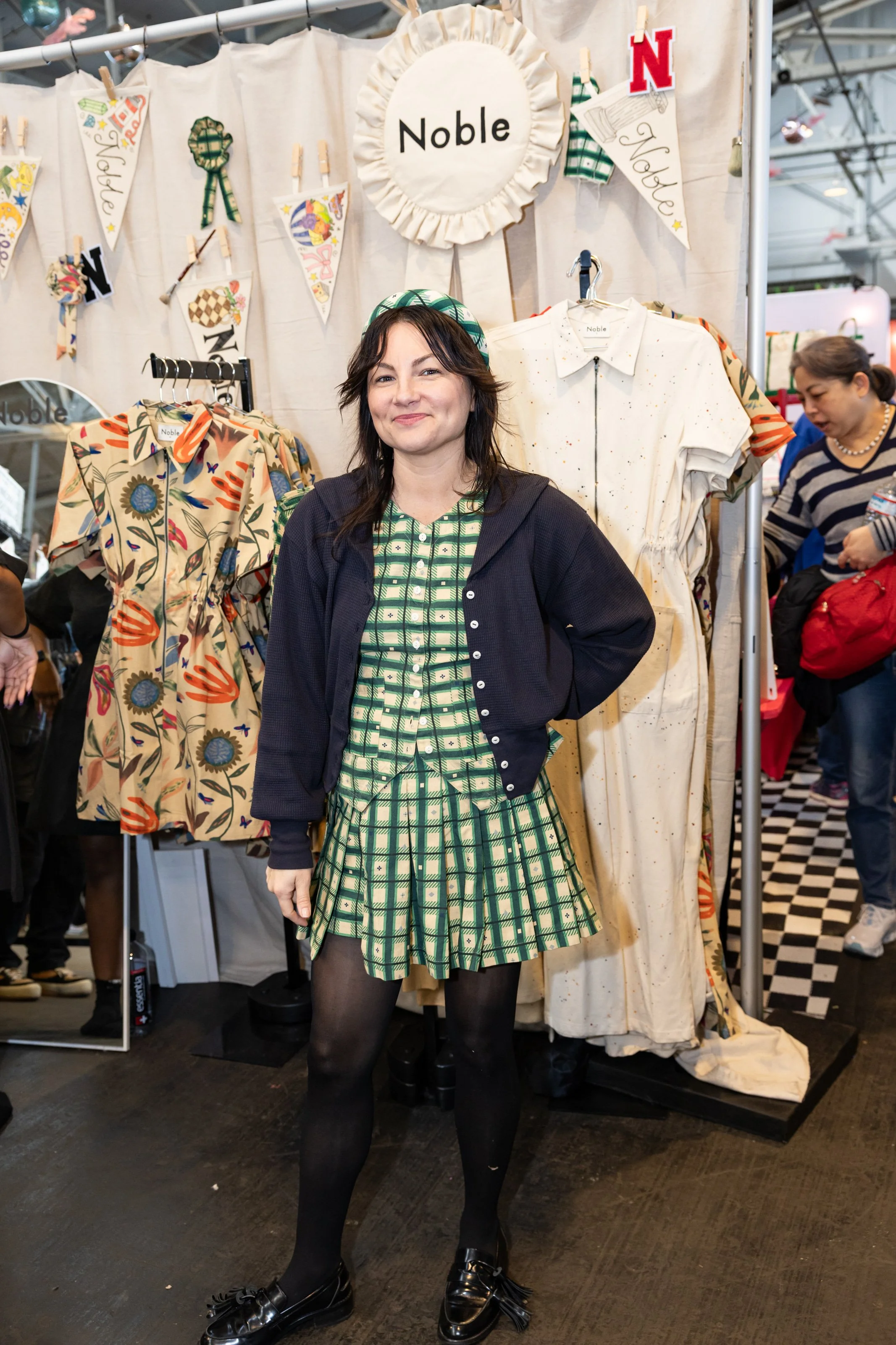Woman standing in front of clothing racks at an indoor craft. show.