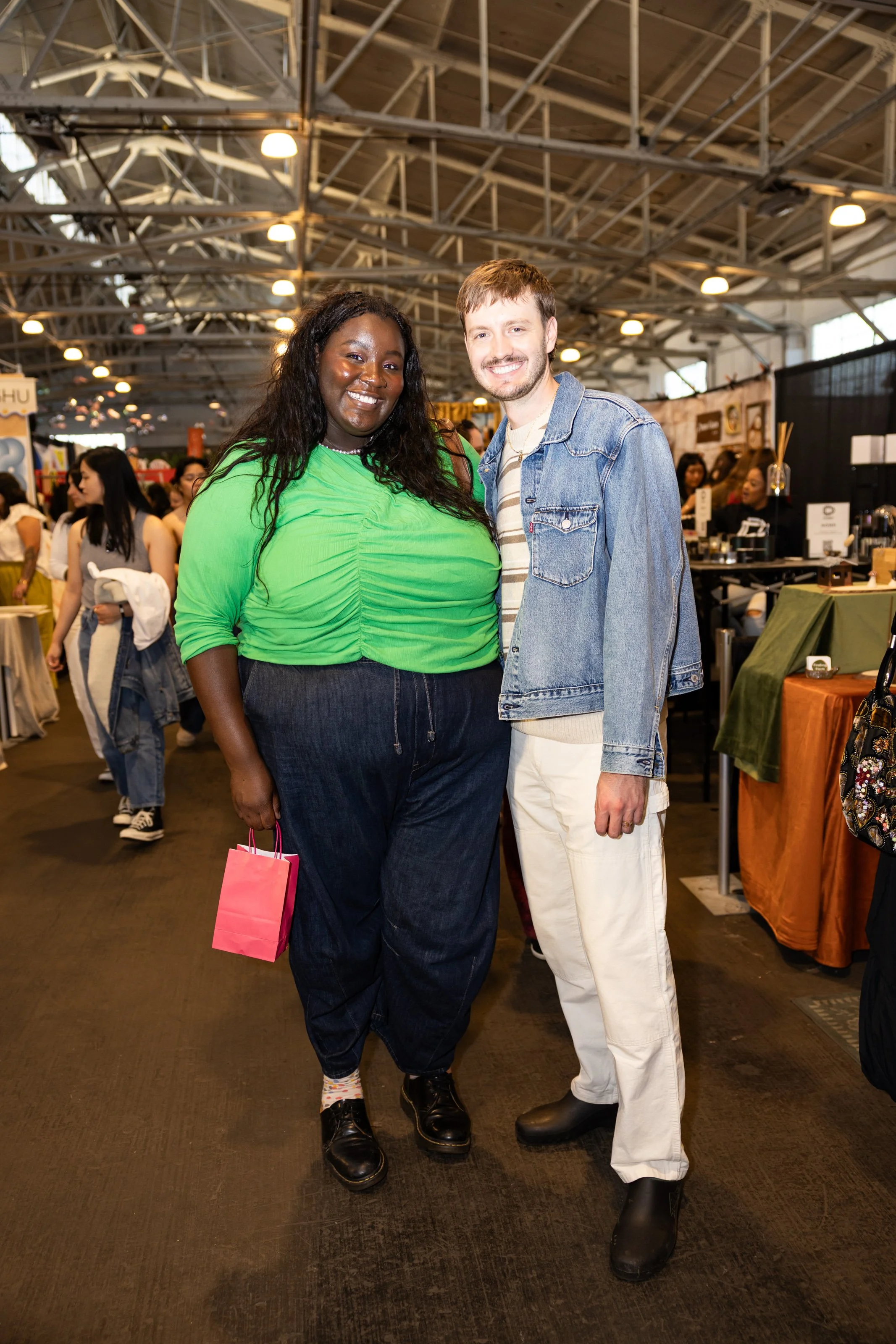 Two friends posing inside an indoor craft show.