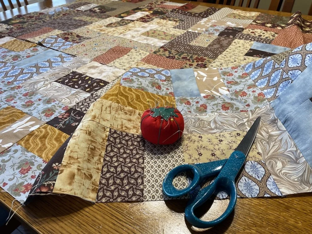 Pieces of a quilt in progress, along with a pin cushion and sewing scissors