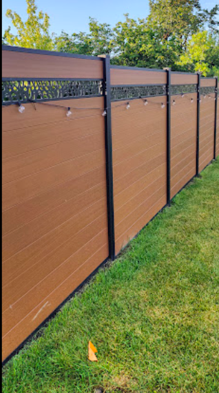 A brown privacy fence with black metal posts, located next to a grassy yard with trees in the background.