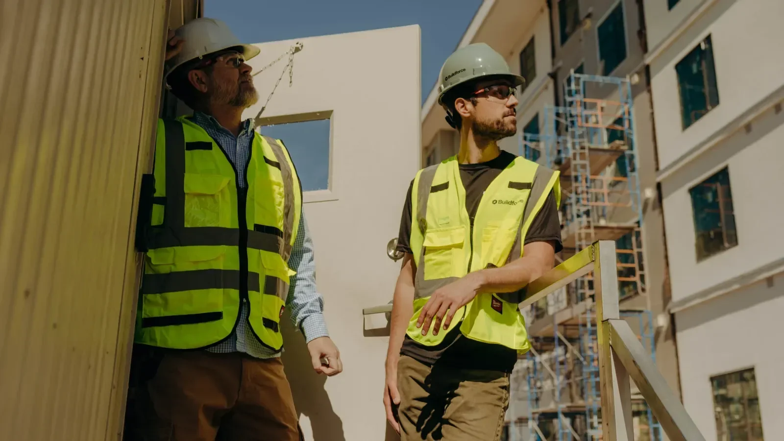 two men with construction vests and hard hats looking at a building