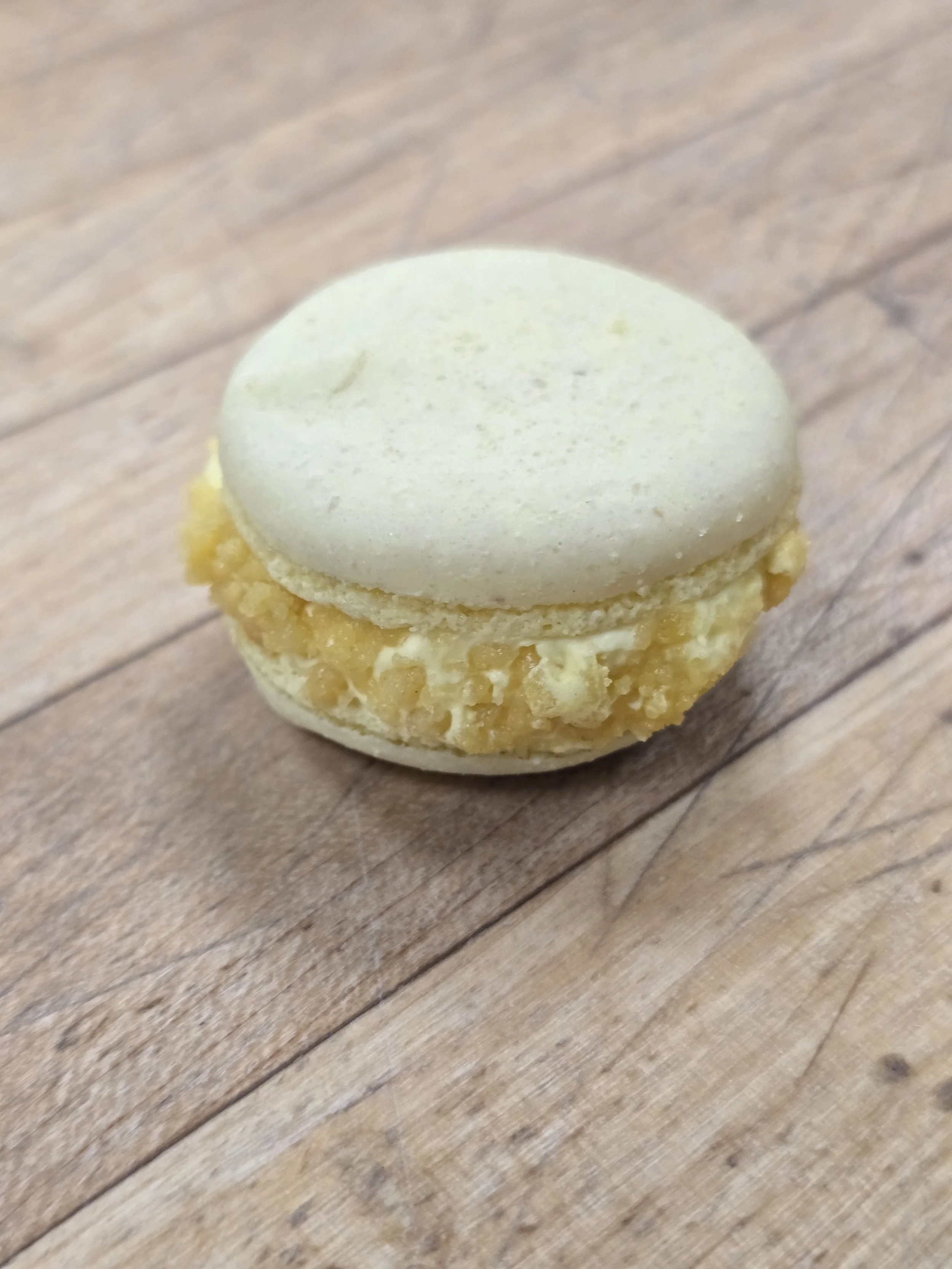 A close-up of a lemon macaron on a wooden surface.