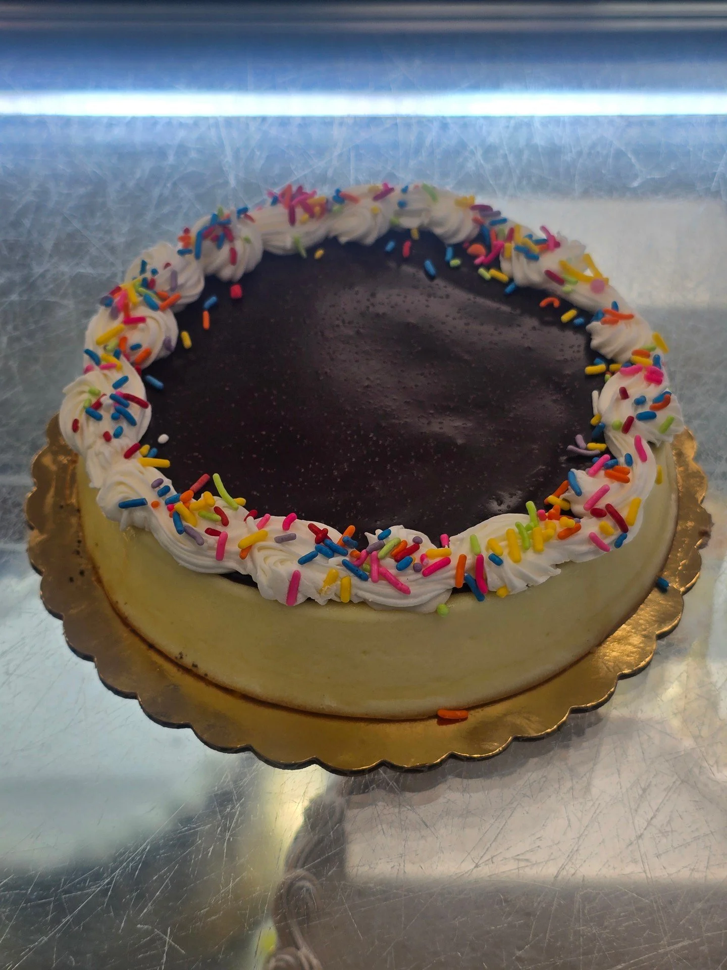 Plain cheesecake topped with chocolate ganache and garnished with a frosting boarder and sprinkles #antoinespastryshop #cheesecake #plaincheesecake #frosting #ganache #chocolate #rainbowsprinkles