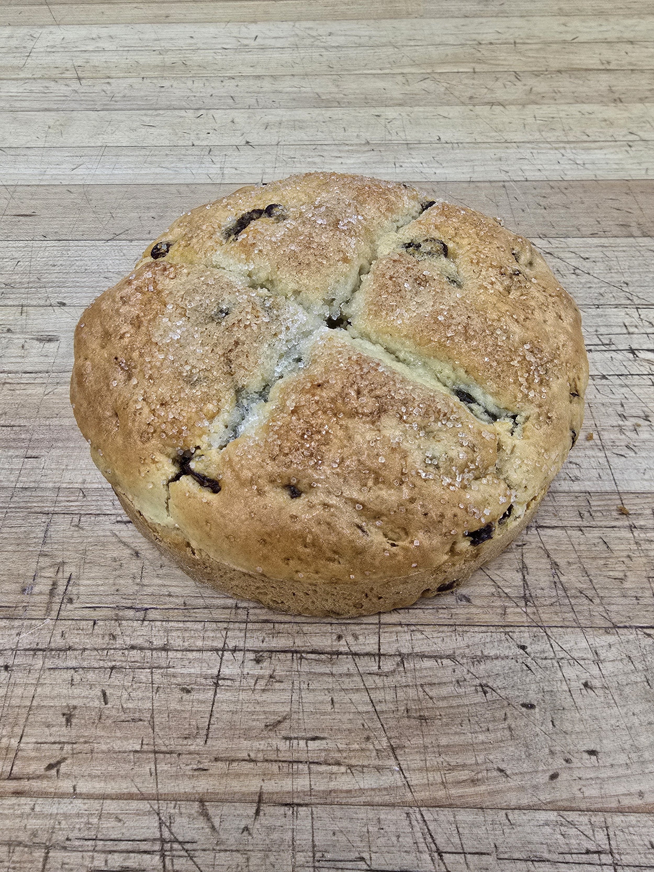 A round chocolate chip cookie on a wooden surface.
