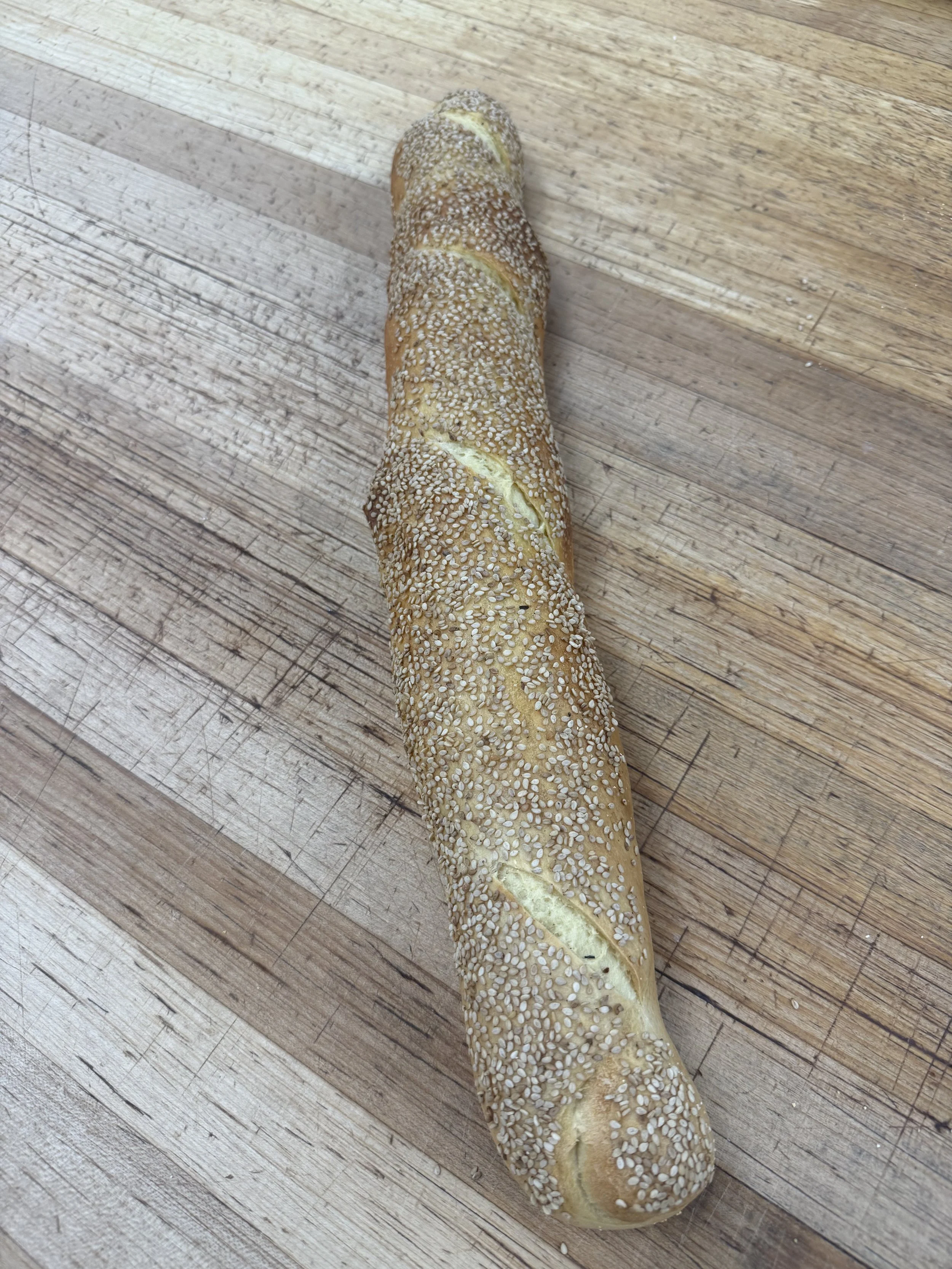 UnCut bread roll covered with sesame seeds on a wooden surface.