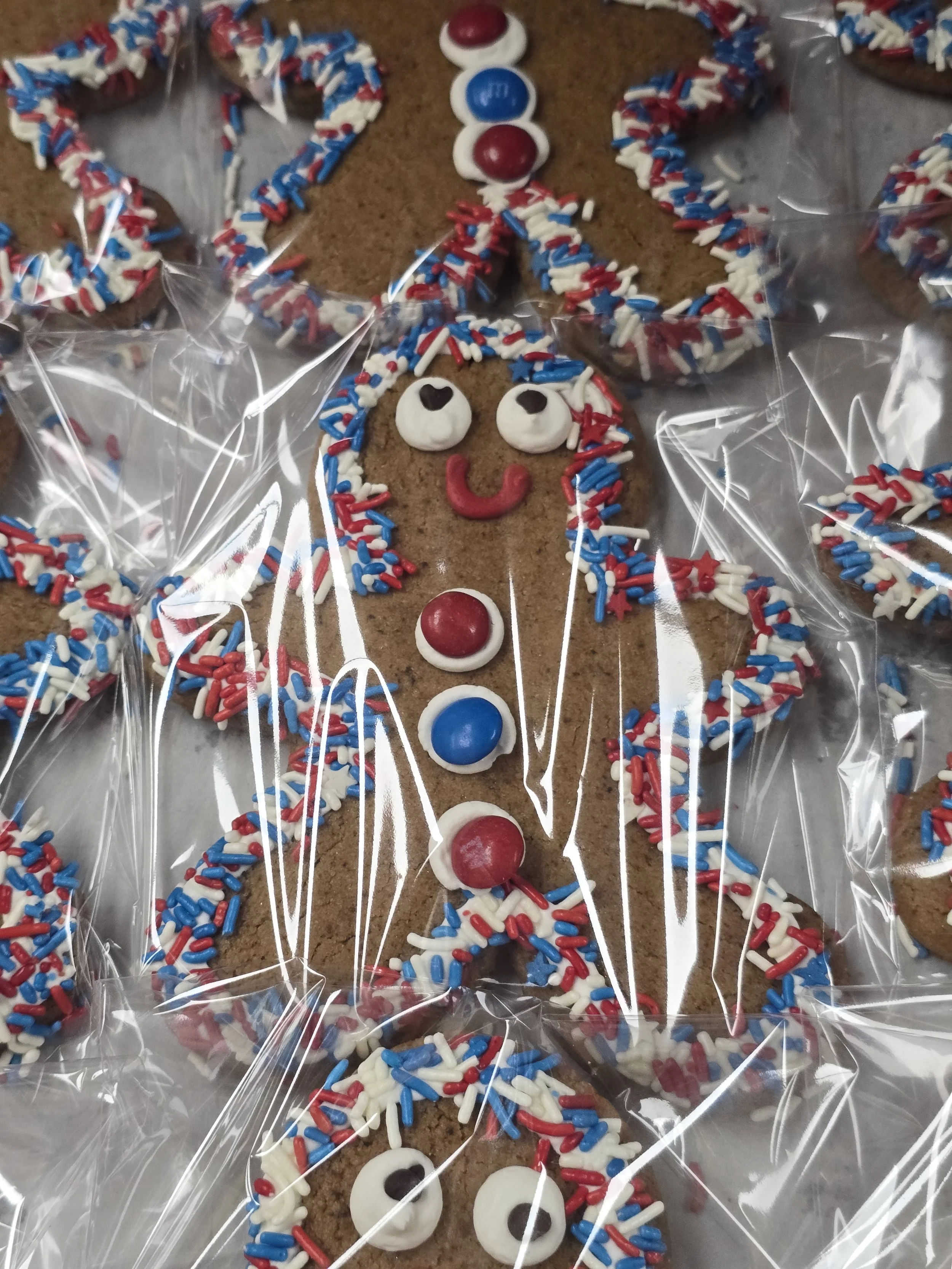 Fourth of july decorated cookies in shamrock and leprechaun shapes, wrapped in clear plastic, with green, white, and orange sprinkles and icing.