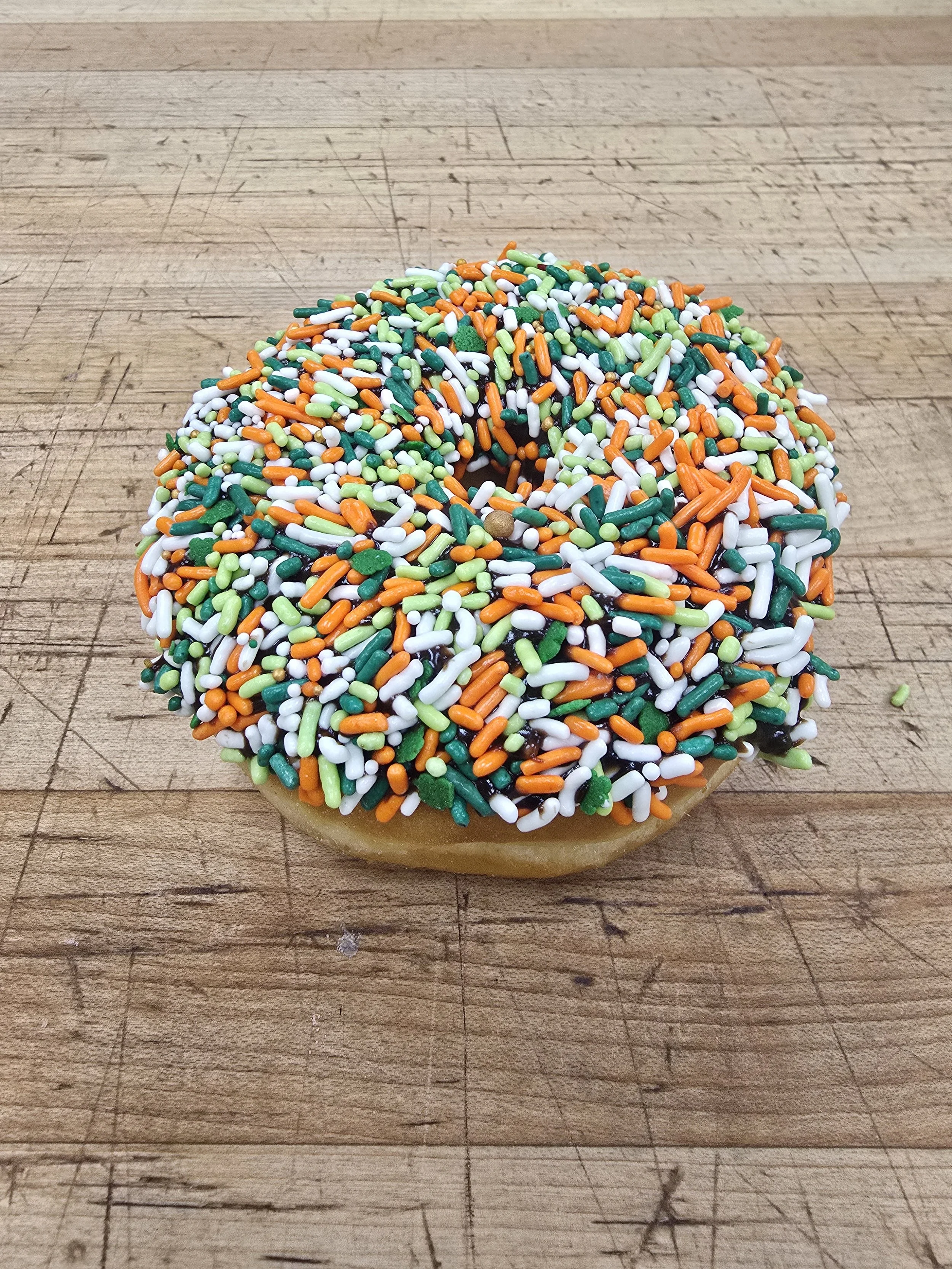 A donut covered with multicolored sprinkles, sitting on a wooden surface.