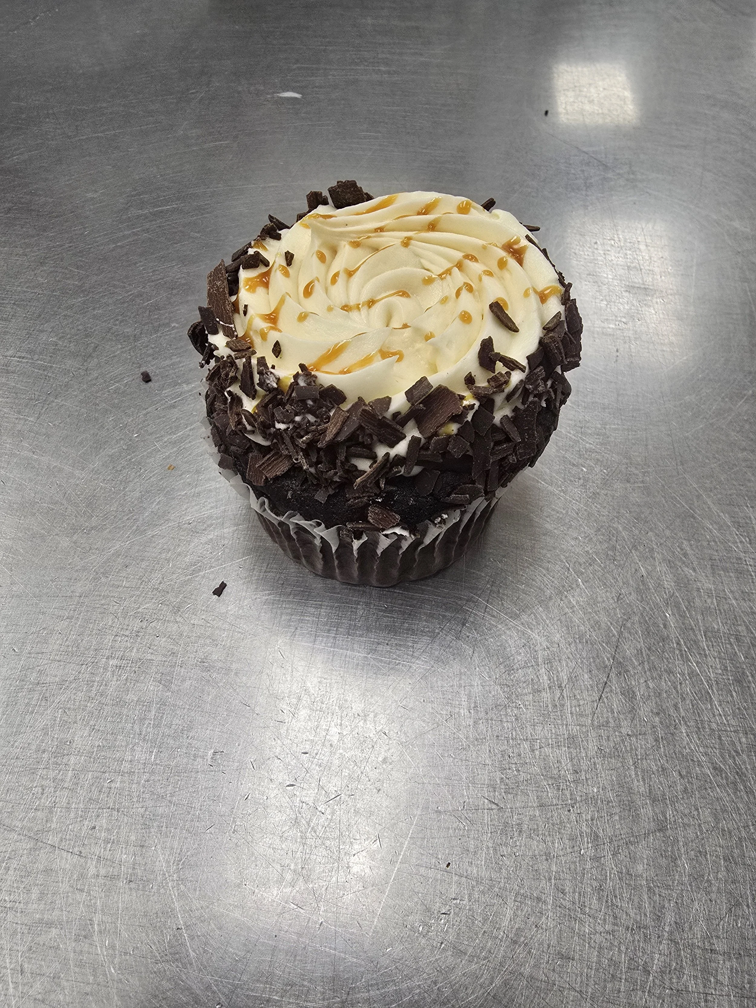 Chocolate cupcake with white frosting, drizzled with chocolate sauce, topped with a small chocolate piece, on a wooden surface.