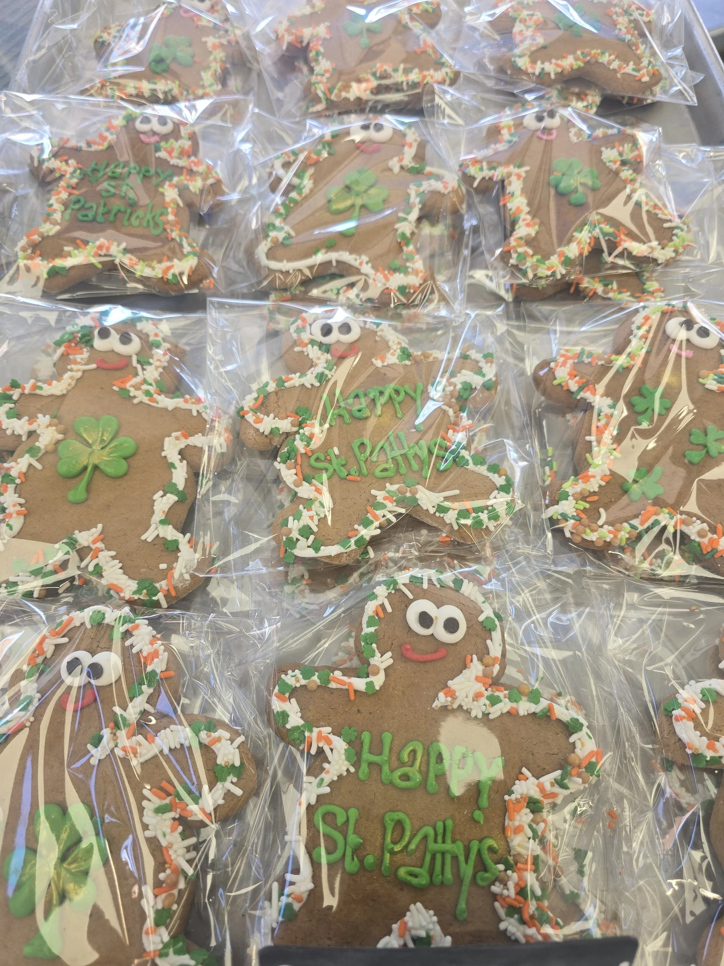 St. Patrick's Day decorated cookies in shamrock and leprechaun shapes, wrapped in clear plastic, with green, white, and orange sprinkles and icing.