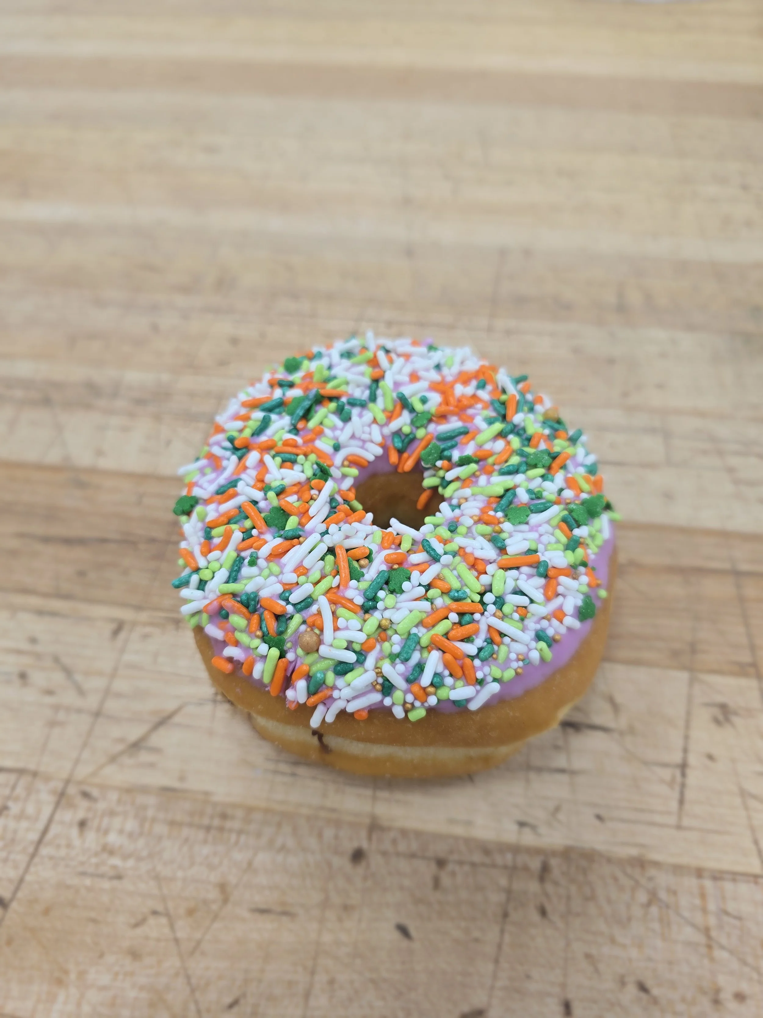 Pink frosted donut with multicolored sprinkles on a wooden surface.