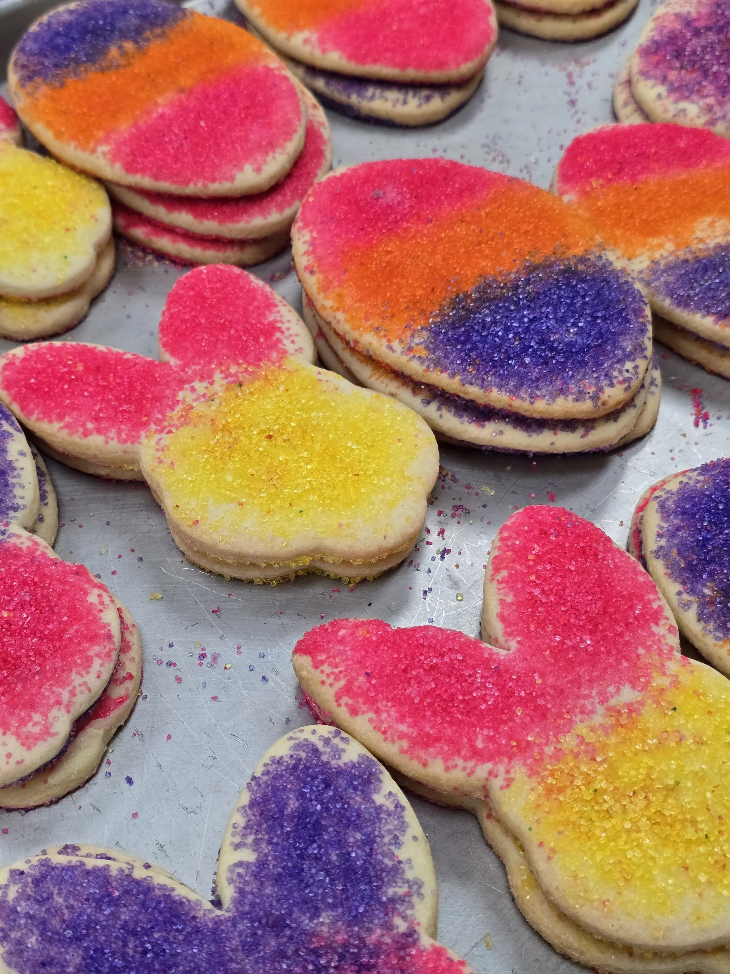 Cookies shaped like shamrocks with green sugar sprinkles on top, placed on a silver baking sheet.