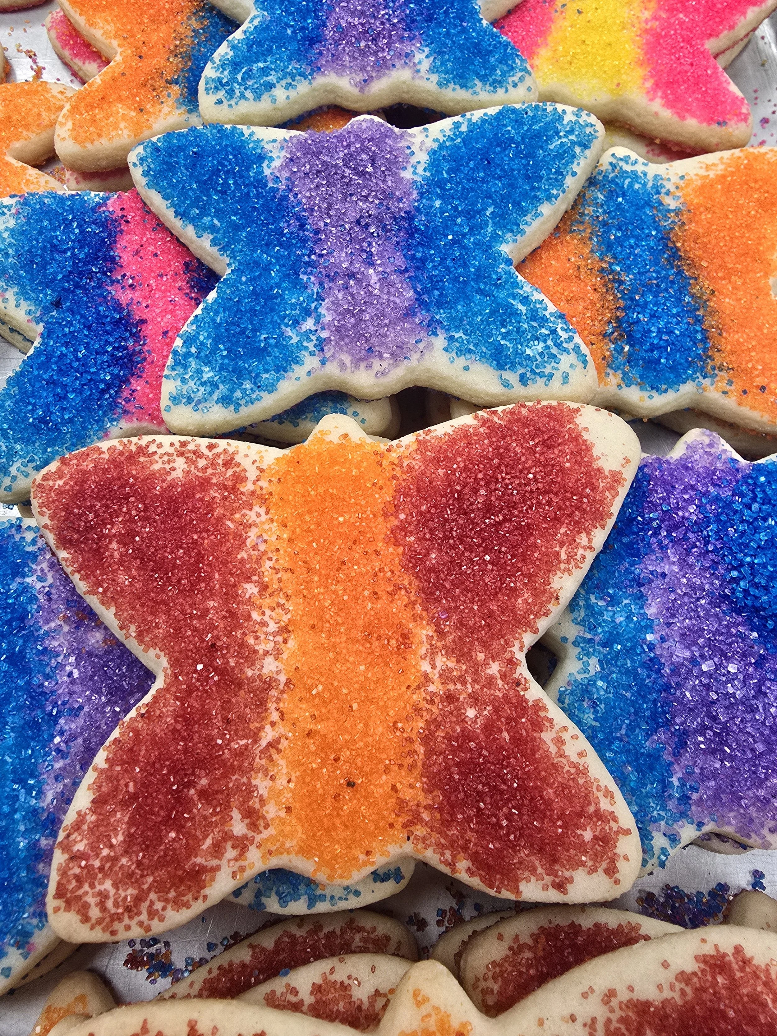 Cookies shaped like shamrocks with green sugar sprinkles on top, placed on a silver baking sheet.